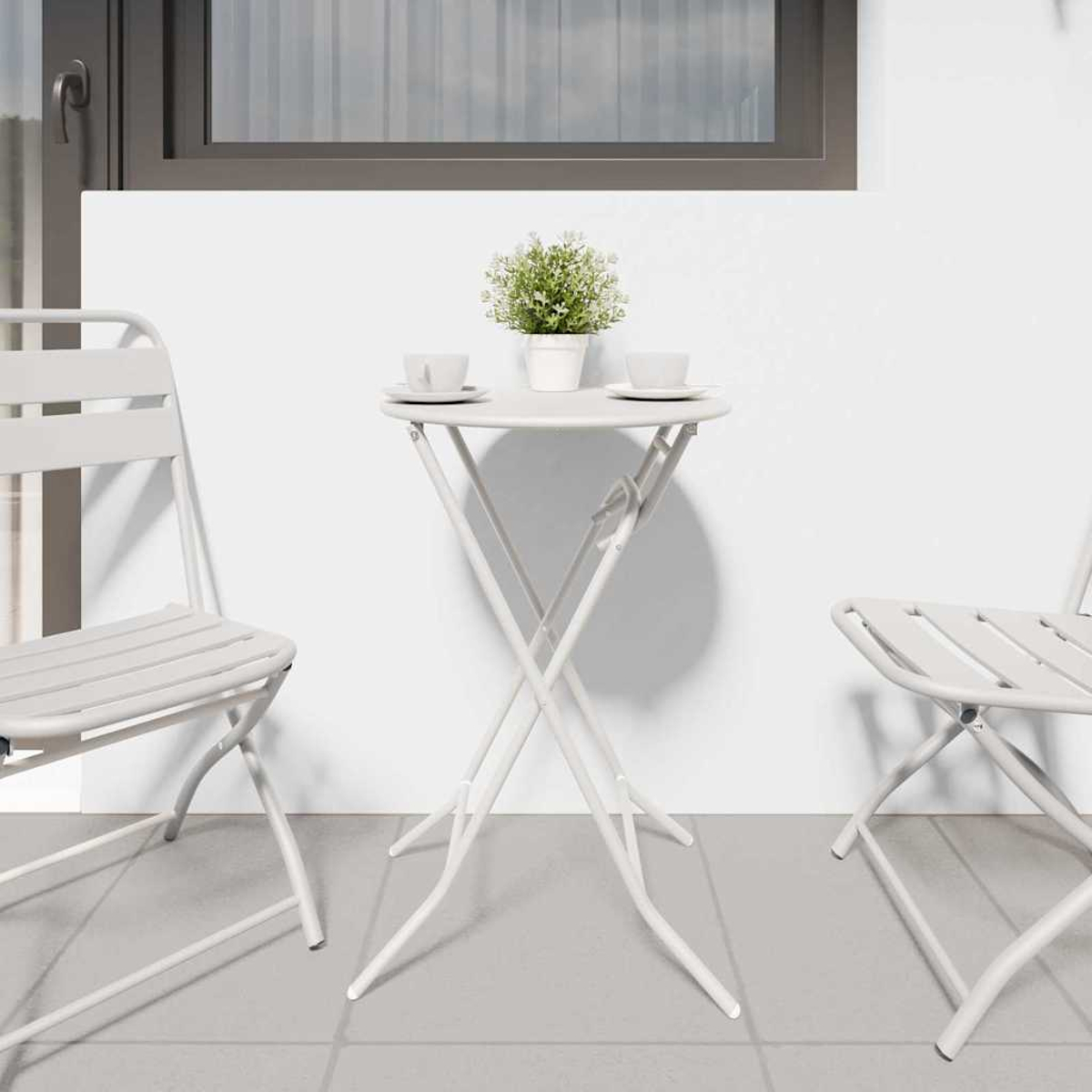 Ein weißer Tisch mit einer Pflanze und zwei Tassen, flankiert von zwei weißen Stühlen, steht auf einer gefliesten Terrasse. Im Hintergrund ist ein Fenster.