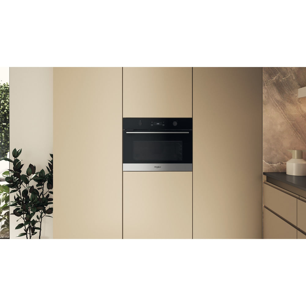 Forno a incasso in una cucina. Mobili beige circondano il forno. Una pianta è nell'angolo sinistro. Il forno ha una porta nera e una maniglia argentata.