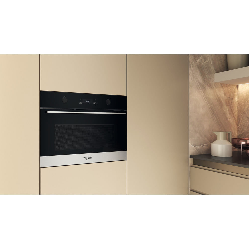 Un forno nero a incasso con finiture in acciaio inossidabile è montato in un mobile da cucina beige. A destra è visibile una brocca bianca.