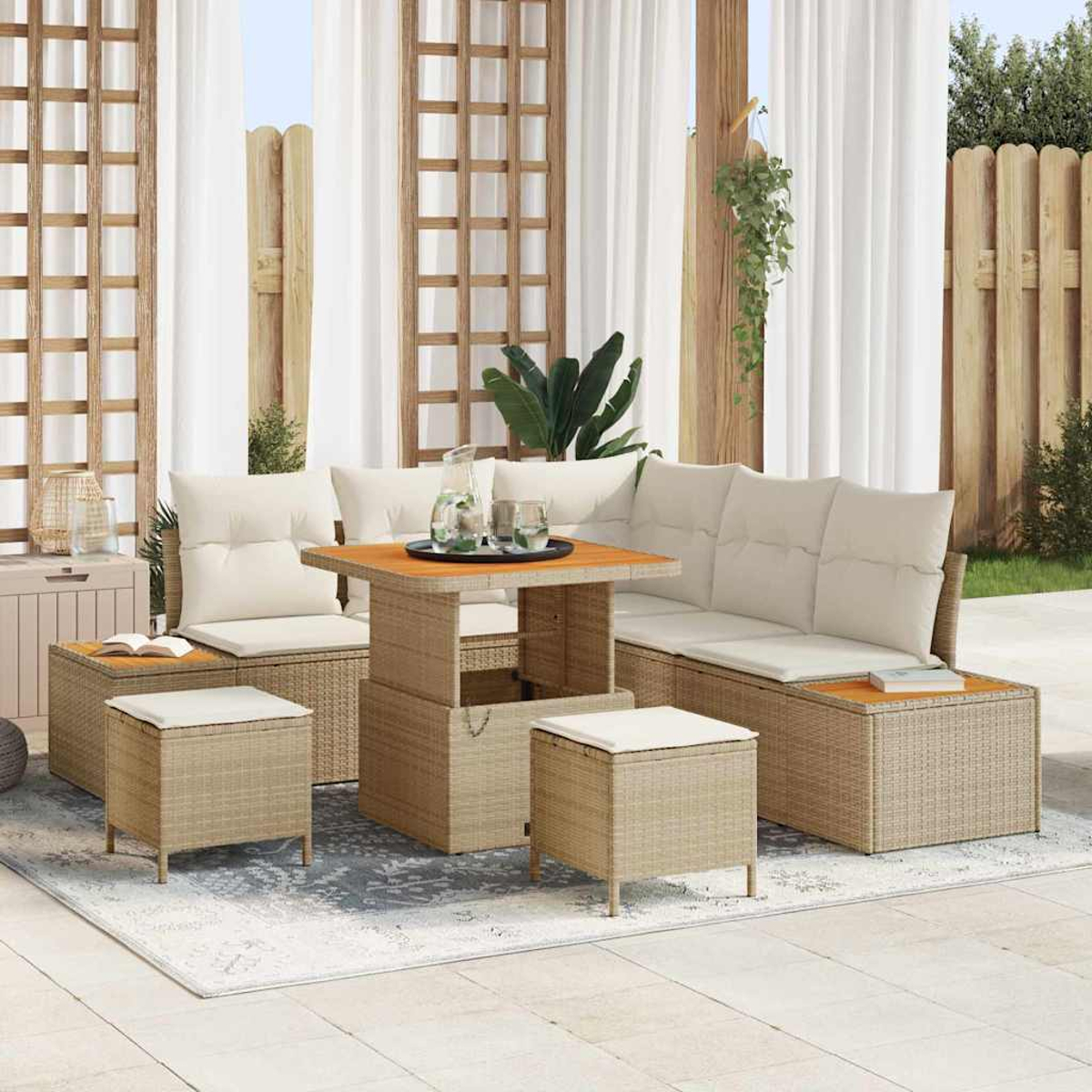 Gartenmöbel-Set aus Rattan mit beigen Kissen. Enthält einen Tisch, ein Sofa und Hocker. Weiße Vorhänge und Holzzaun im Hintergrund.