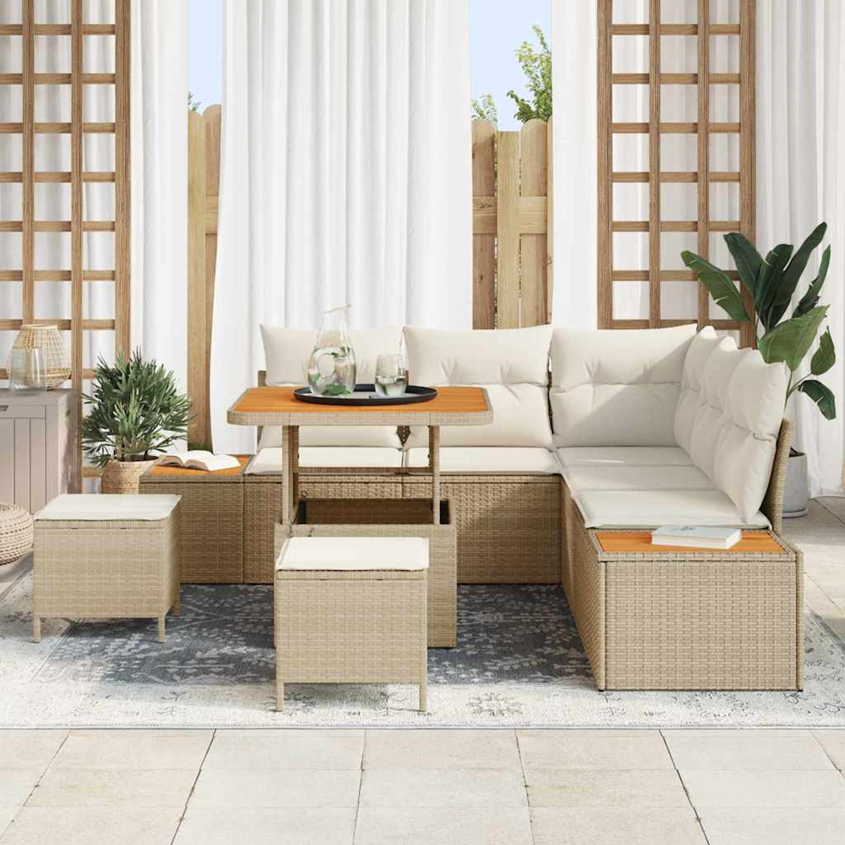 Outdoor-Sitzbereich mit beigen Korbmöbeln, weißen Kissen und einem kleinen Tisch mit Getränken. Hintergrund sind Vorhänge und Pflanzen.