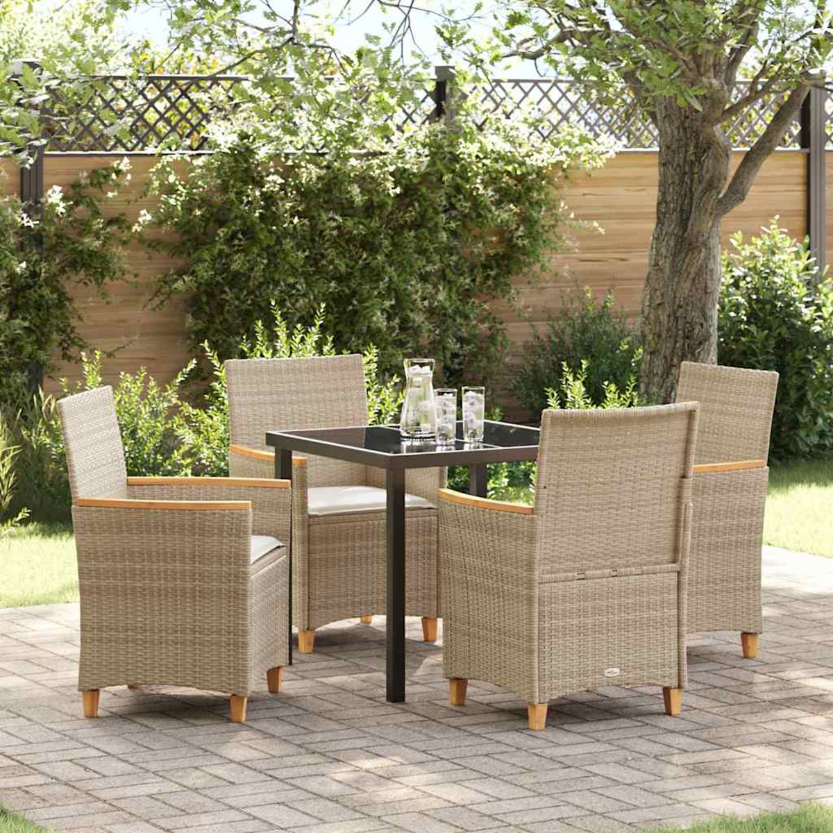 Vier Korbstühle um einen quadratischen Tisch mit Getränken, auf einer gepflasterten Terrasse, umgeben von Grün und einem Holzzaun.