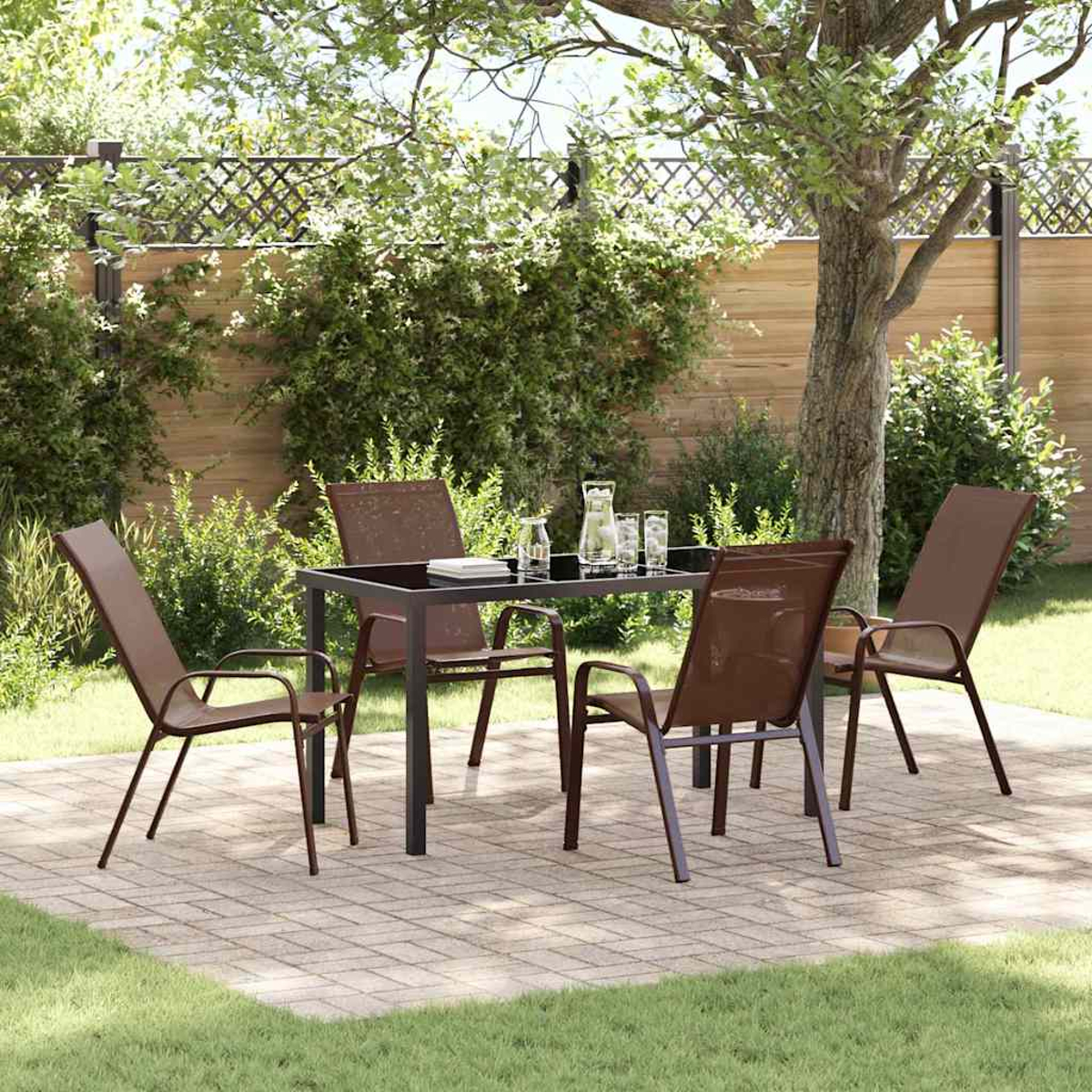 Un set da patio con tavolo e sedie si trova su un patio in mattoni. Erba verde e una staccionata in legno sullo sfondo.