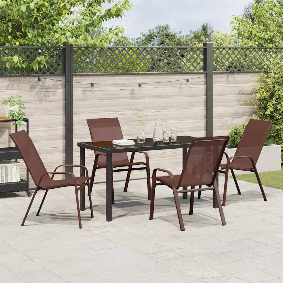 Set da pranzo all'aperto con tavolo, quattro sedie e una recinzione decorativa sullo sfondo. Le sedie sono di colore marrone scuro.