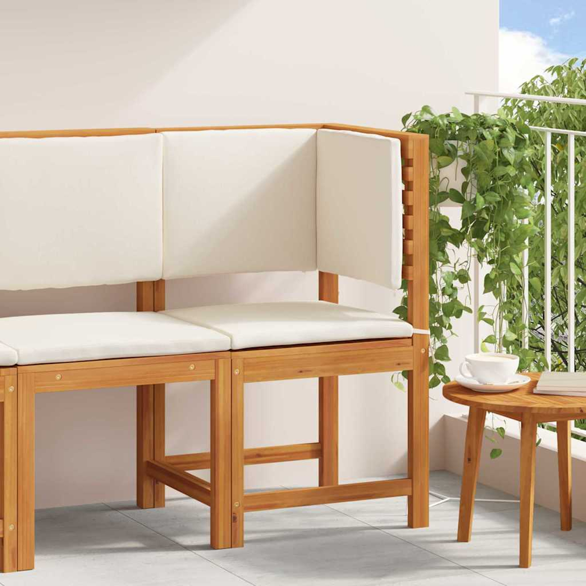 Banco de madera con cojines blancos. Una pequeña mesa con café y un libro junto a él. Plantas verdes en el fondo.