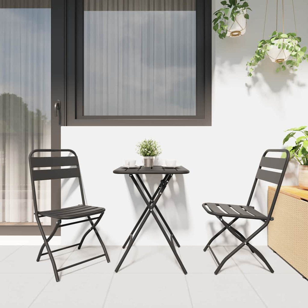 Balkonszene mit schwarzem Tisch und Stühlen. Ein Blumentopf steht auf dem Tisch. Hängepflanzen und Fenster im Hintergrund.