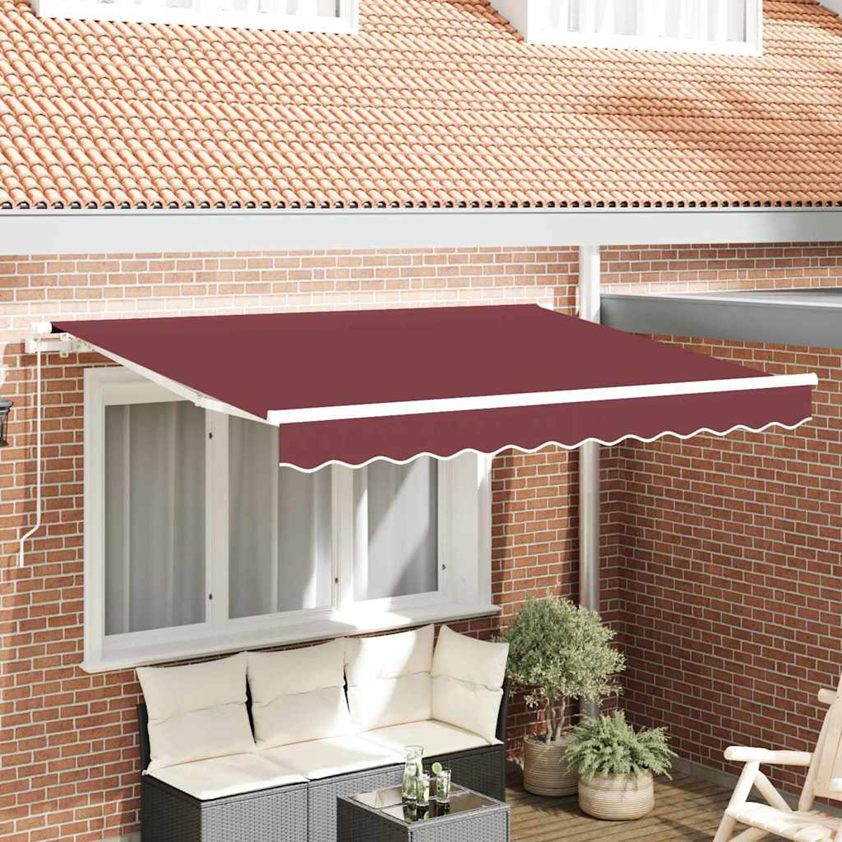 Un toldo granate cubre una ventana. Debajo, un sofá, una mesa y plantas en un patio contra una pared de ladrillo.