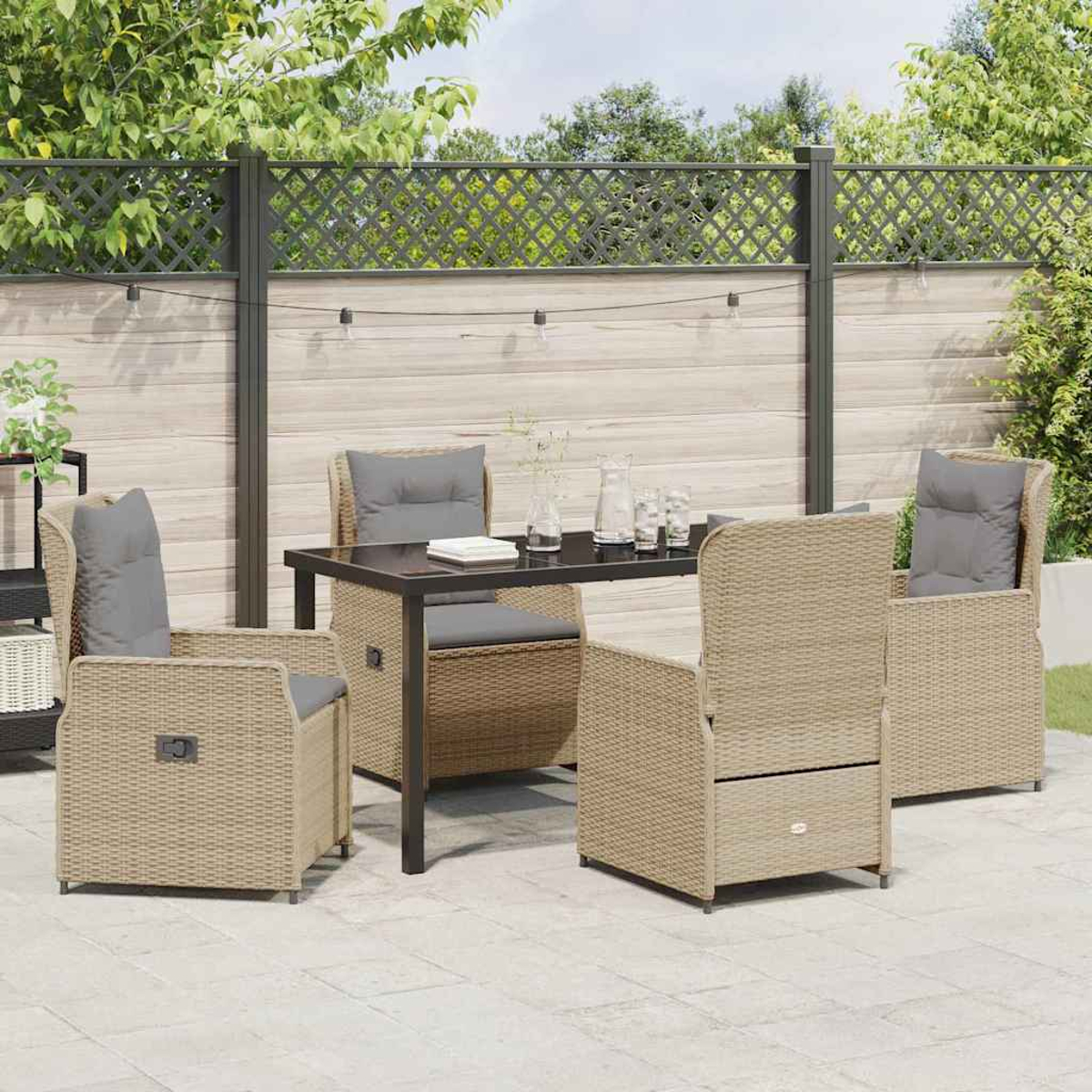 Garten-Sitzgruppe: vier Korbstühle mit grauen Kissen um einen Tisch. Im Hintergrund ein Zaun und Grün.