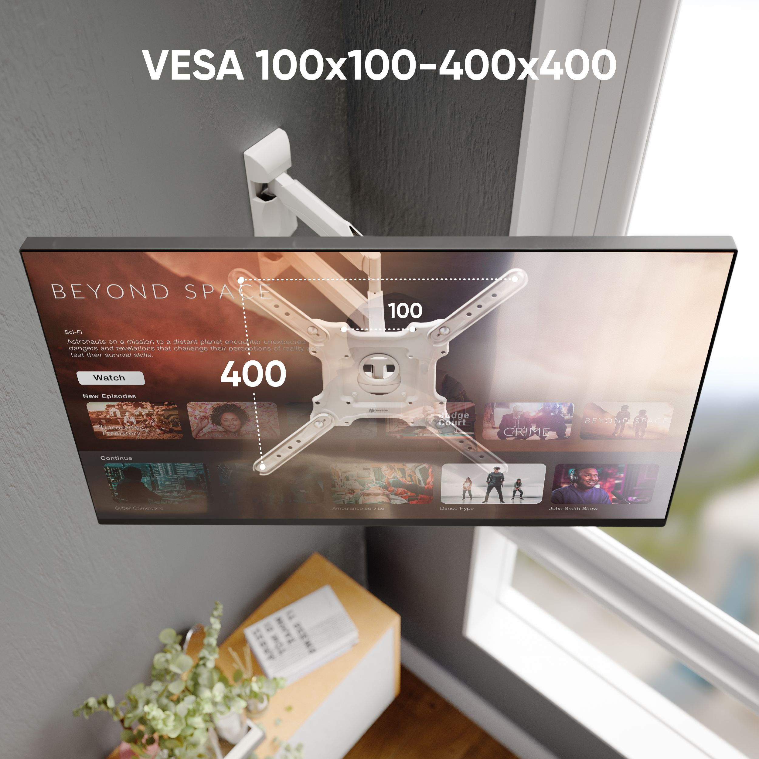 Telewizor zamontowany na ścianie pokazuje usługę przesyłania strumieniowego. Wyświetlane są specyfikacje VESA. Na podłodze stoi mały stolik z książką i rośliną.