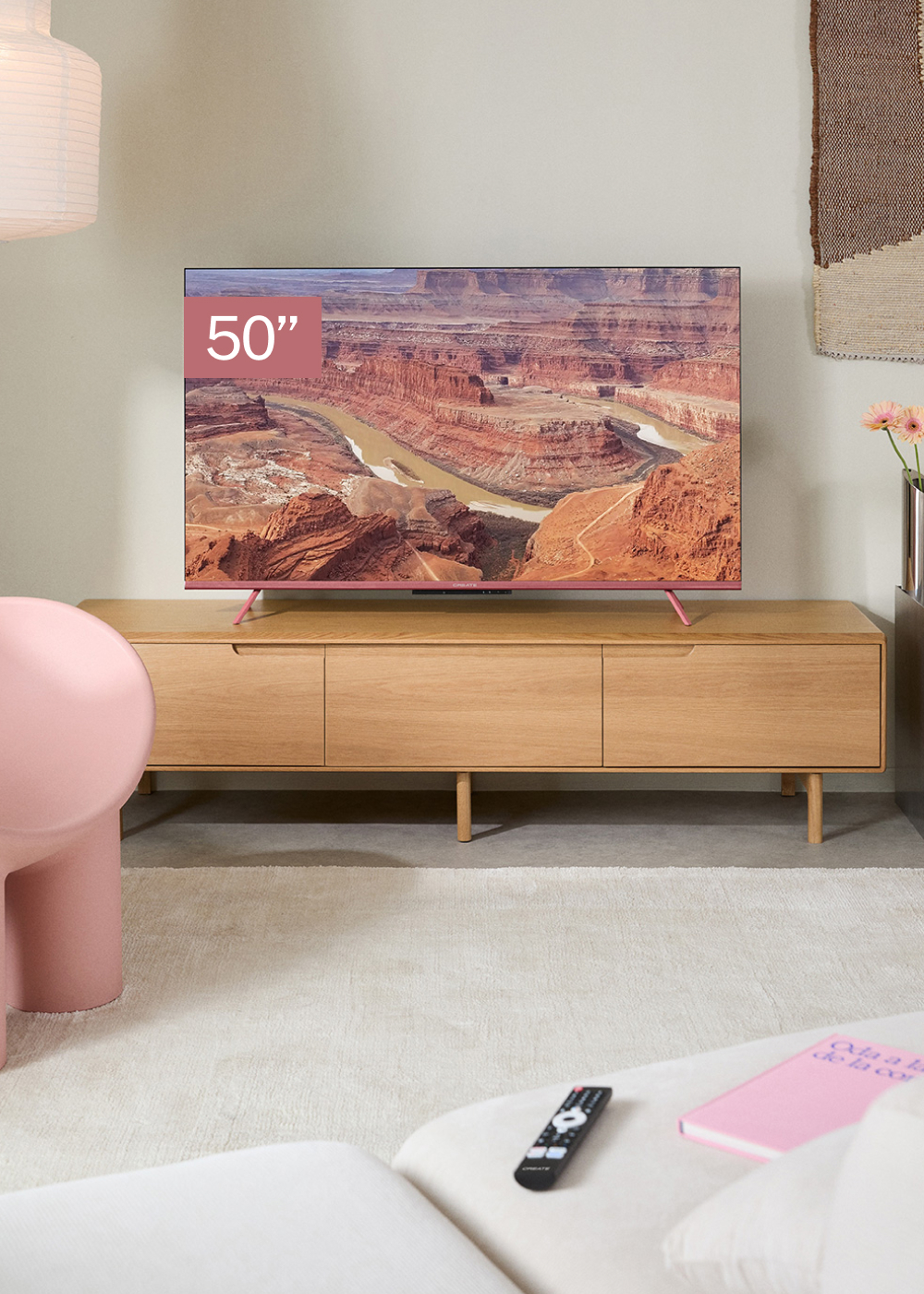 Un televisor de 50" muestra un cañón. Está sobre un mueble de madera. Una silla rosa, un mando y un libro rosa están en primer plano.