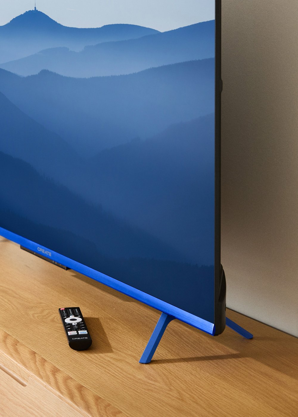 Un televisor azul muestra una escena de montaña. Un mando a distancia negro está sobre una mesa de madera. Las patas del televisor son azules.
