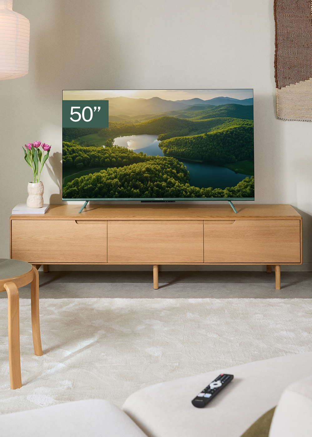 Un televisor de 50" muestra un paisaje sobre un mueble de madera. Un jarrón con tulipanes, una lámpara y un mando a distancia están en la escena.
