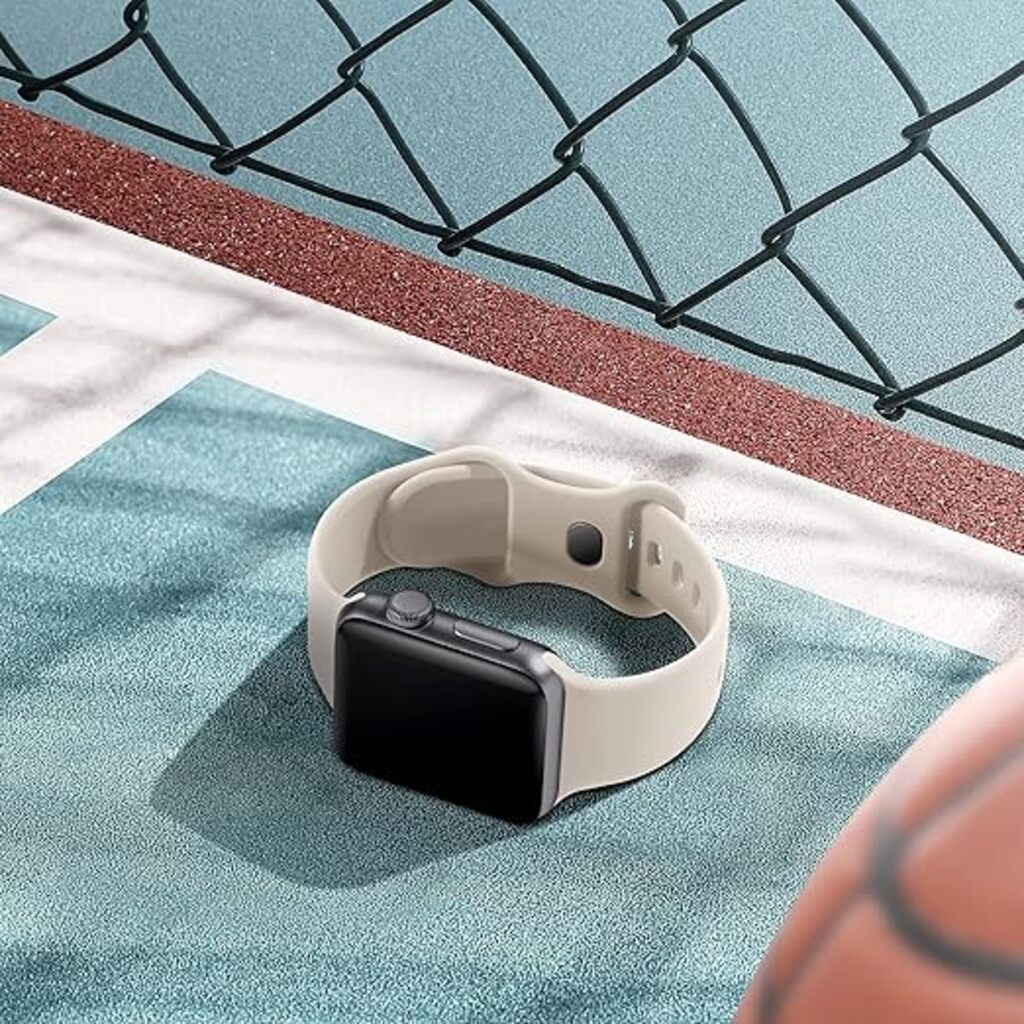 Eine Smartwatch mit schwarzem Bildschirm und beigem Armband liegt auf einer blauen Oberfläche mit rotem Rand und schwarzem Zaun.