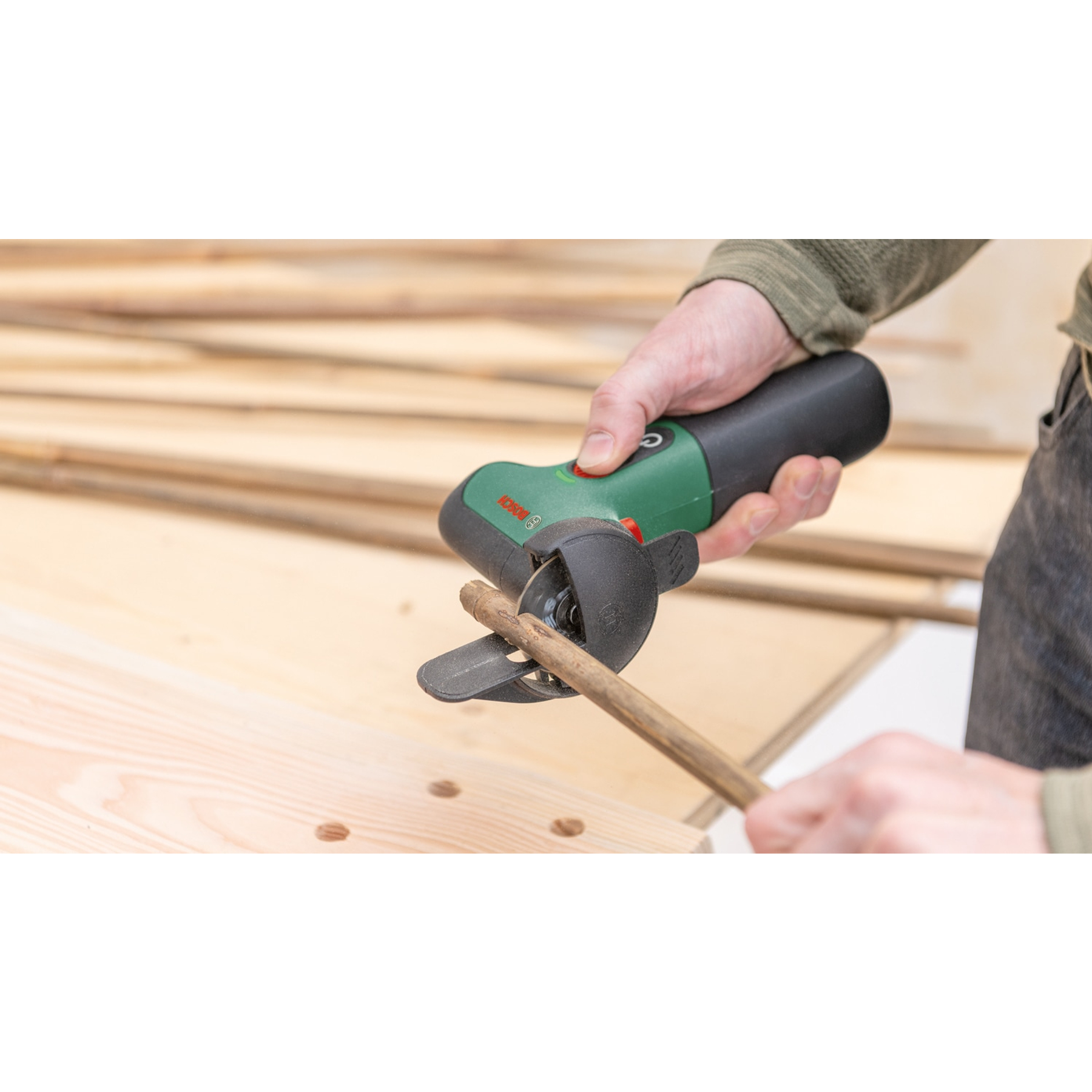 Une personne utilise un outil électrique vert et noir pour couper une cheville en bois. Des morceaux de bois sont sur une surface en bois clair.