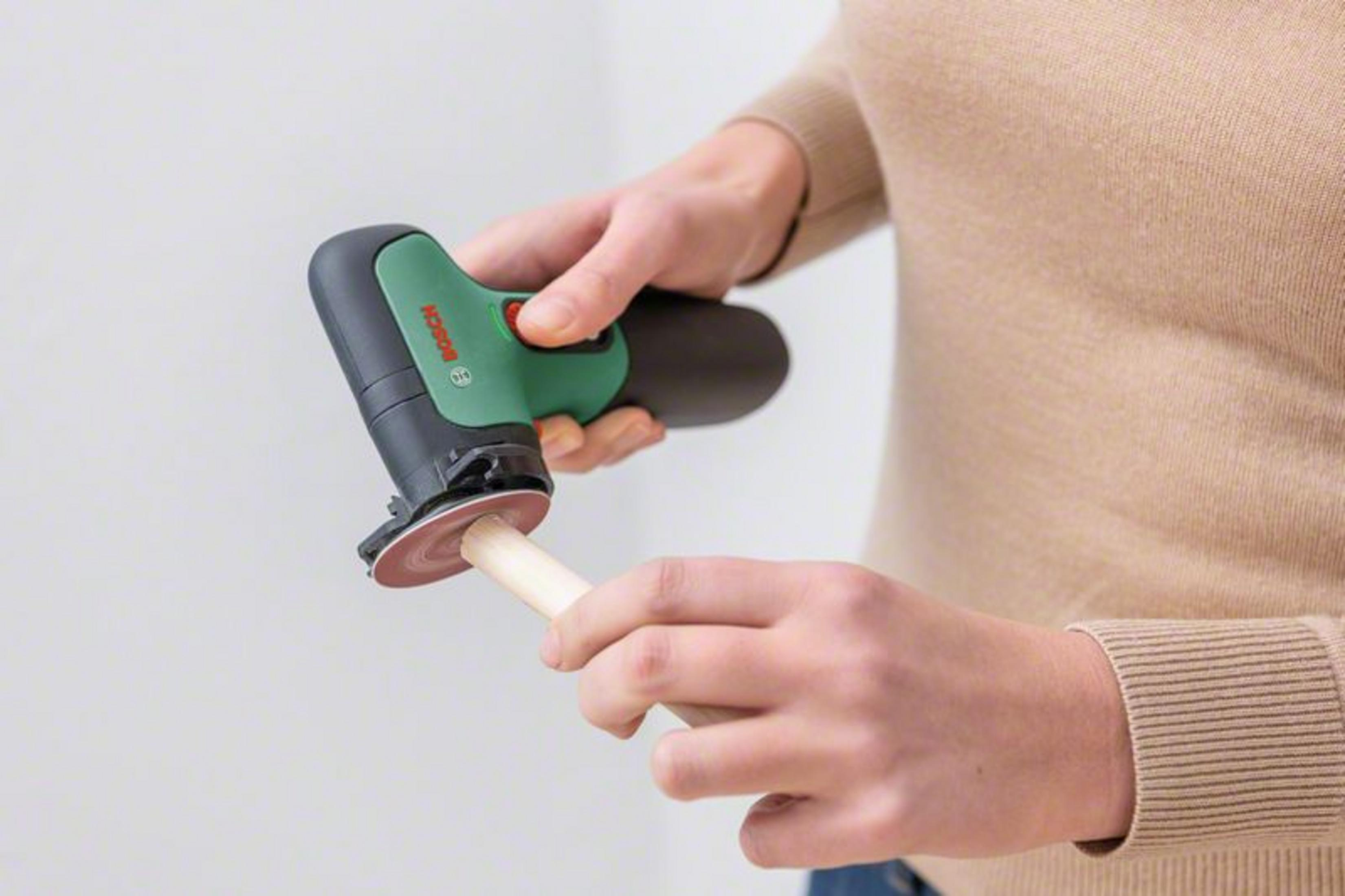 Une personne utilise un outil électrique Bosch pour poncer une cheville en bois. L'outil est noir et vert.