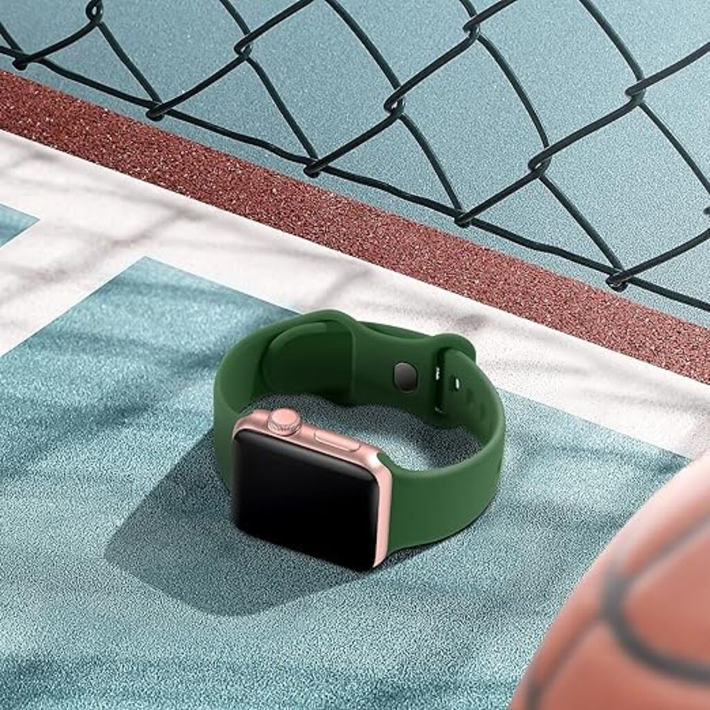 Grüne Smartwatch mit roségoldenem Gehäuse auf blauem Untergrund, mit Zaun im Hintergrund. Die Uhr ist im Fokus.
