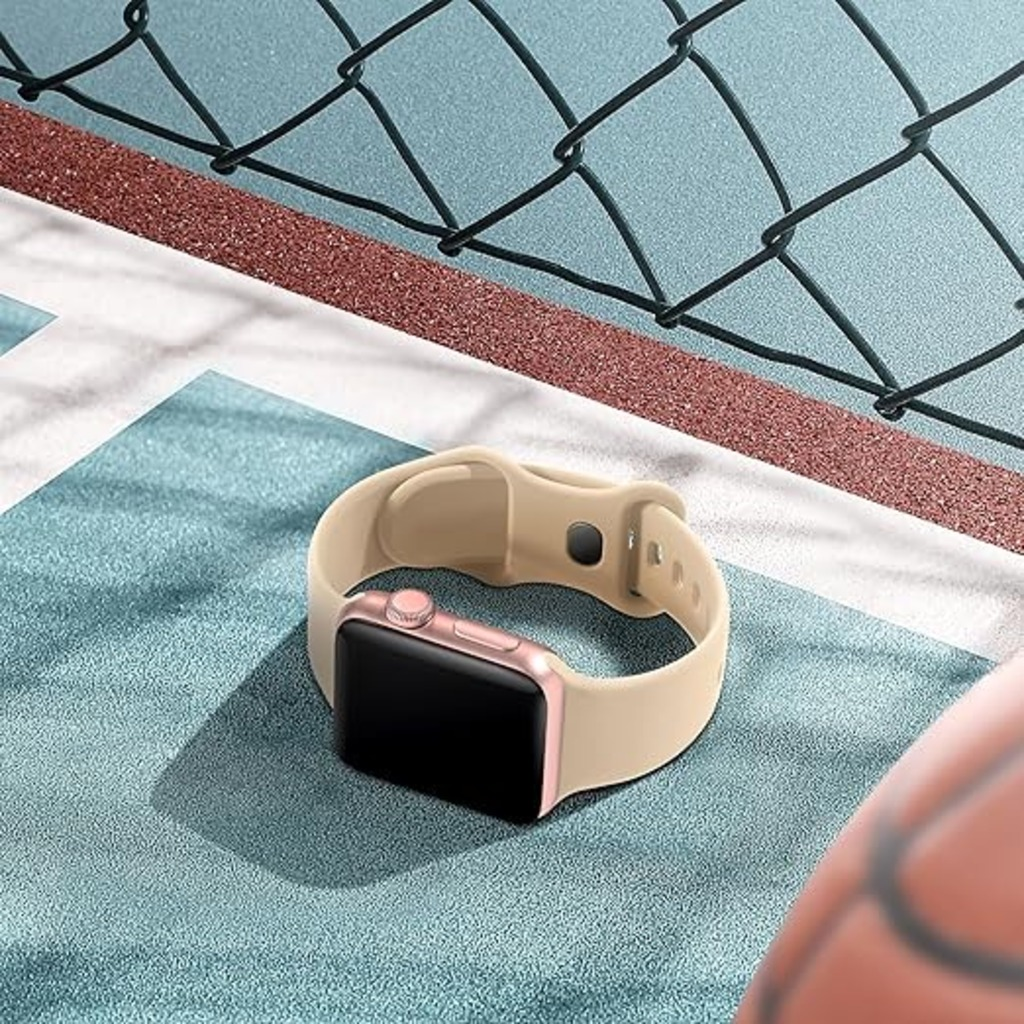 Eine beige Smartwatch mit schwarzem Bildschirm liegt auf einer blauen Oberfläche. Ein Basketball und ein Maschendrahtzaun sind im Hintergrund.
