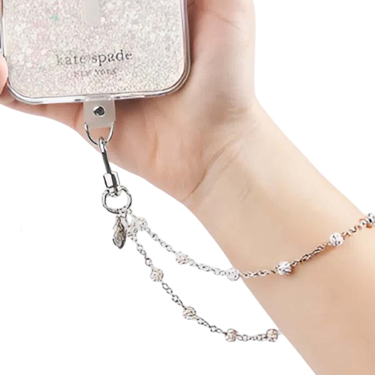 Eine Hand hält eine Kate Spade-Handyhülle mit einem silbernen Riemen. Ein silbernes Kettenarmband ist am Handgelenk.