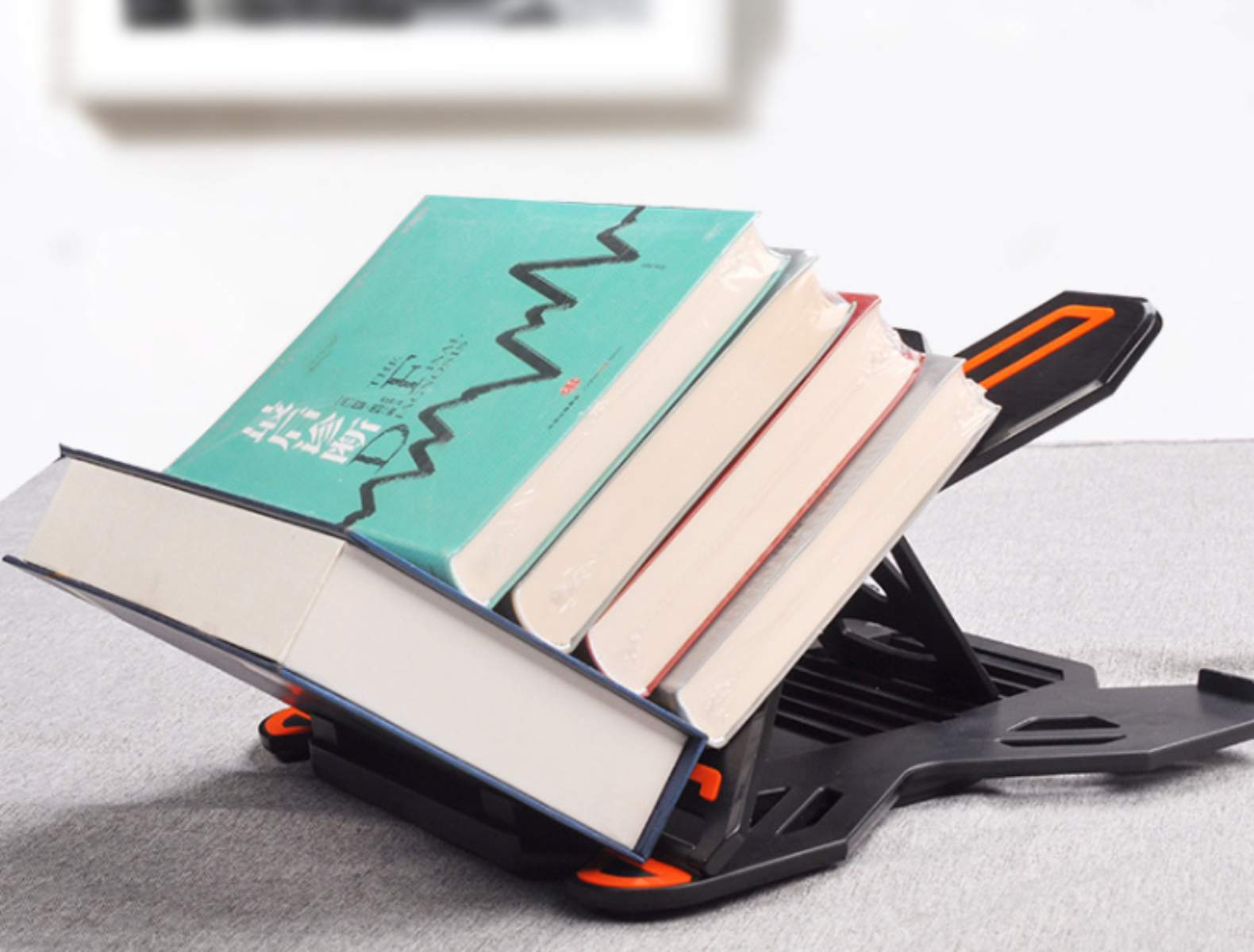 Bücher auf einem schwarzen Buchständer. Die Bücher haben verschiedene Farben. Der Ständer steht auf einer grauen Oberfläche. Eine weiße Wand ist im Hintergrund.