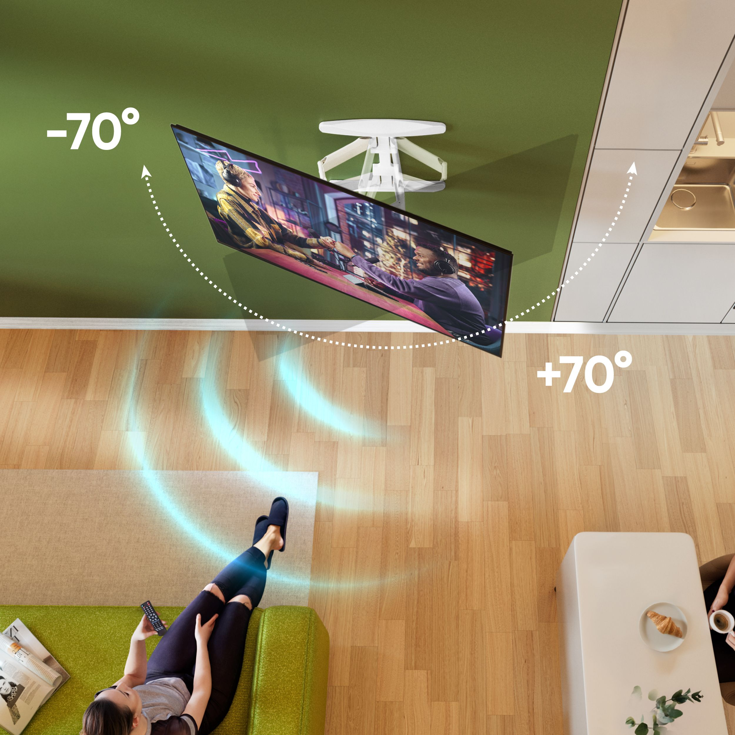 Osoba leży na zielonej kanapie, oglądając telewizję. Telewizor jest zamontowany na suficie. Stół z rogalikiem i kawą po prawej.