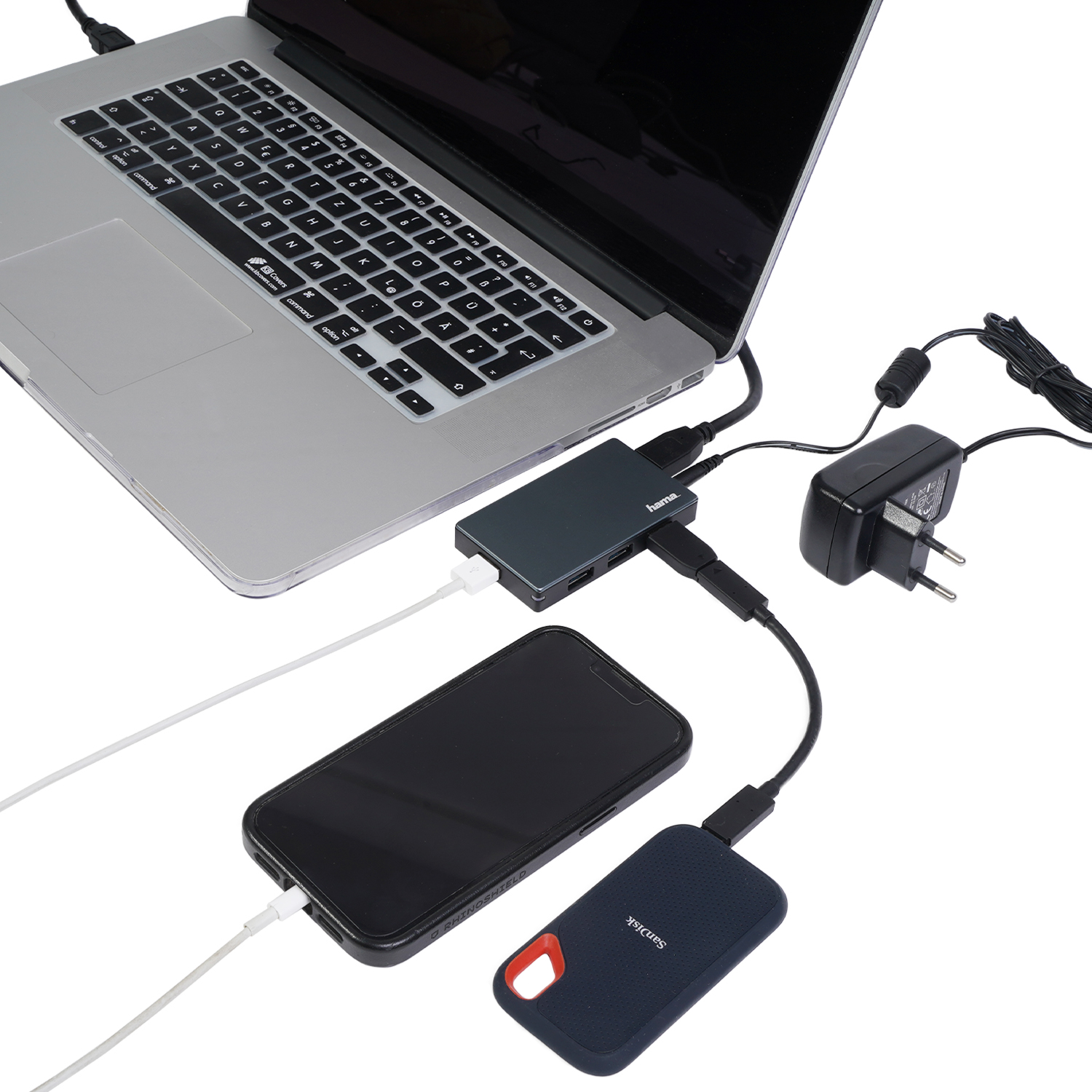 Laptop podłączony do huba, telefonu i zewnętrznego dysku twardego. Zasilacz podłączony. Kable łączą wiele urządzeń.