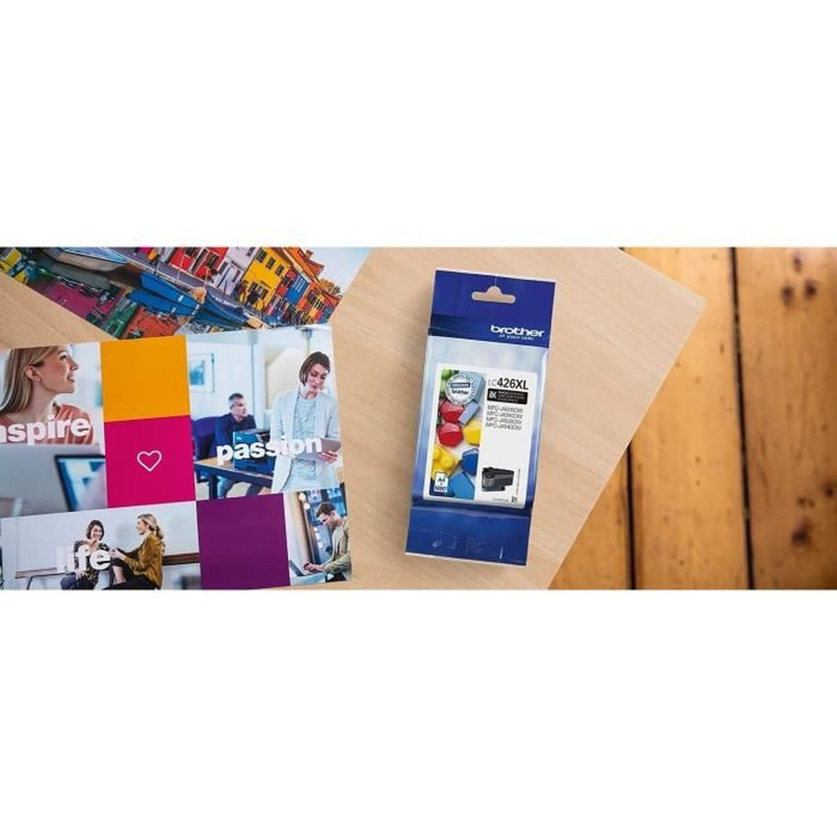 Obraz przedstawia opakowanie z wkładami atramentowymi Brother i kolorowy, inspirujący plakat. Oba elementy znajdują się na drewnianej powierzchni.