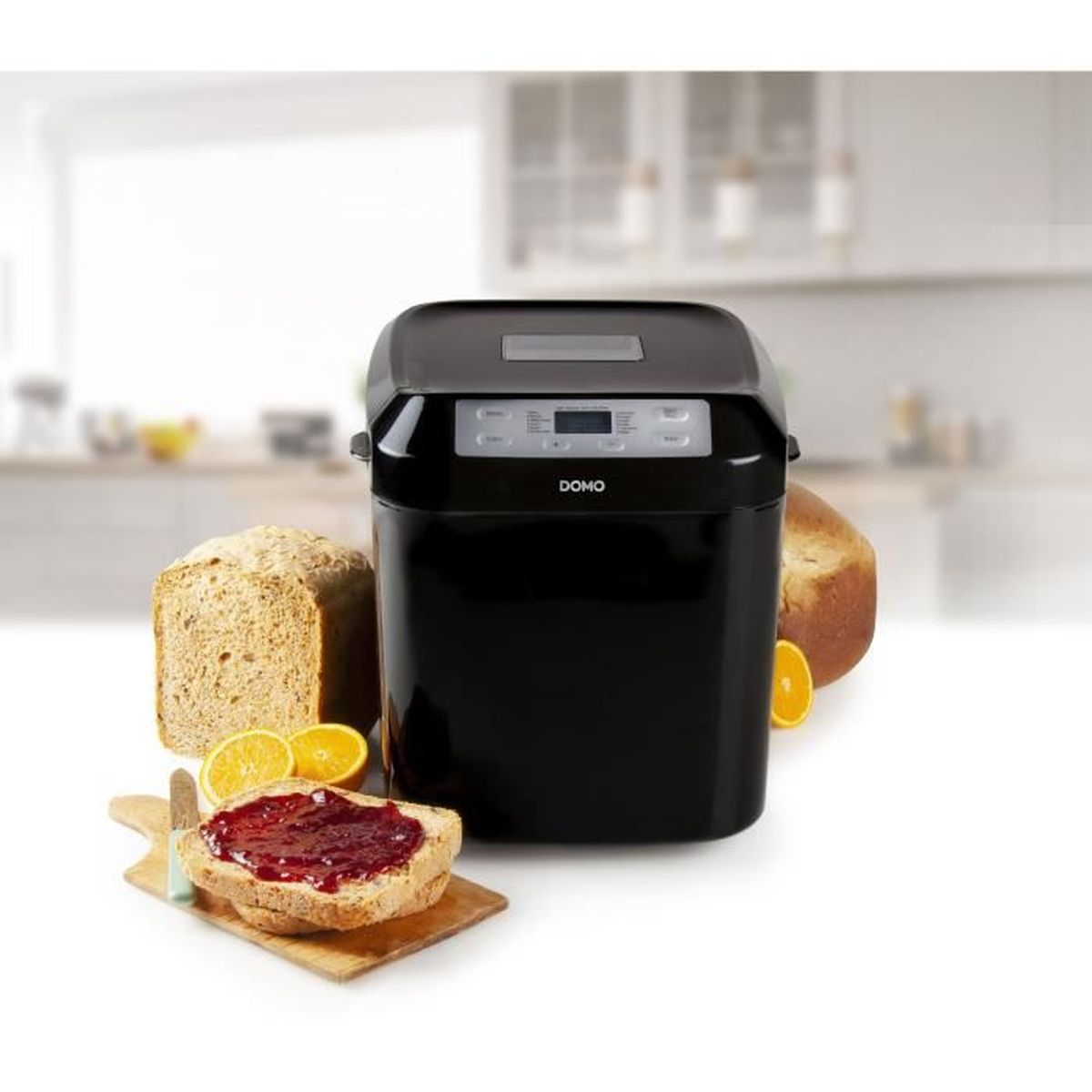 Ein schwarzer Brotbackautomat neben geschnittenem Brot mit Marmelade, Orangen und einem Brotlaib. Küchenhintergrund.
