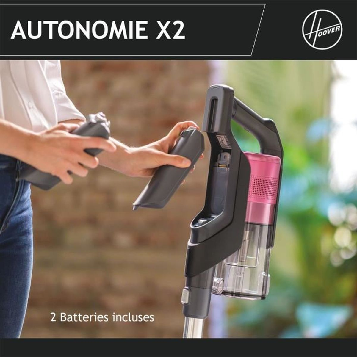 Eine Person legt einen Akku in einen Hoover-Staubsauger ein. Der Staubsauger ist schwarz und rosa. Der Text lautet: 2 Batterien enthalten.