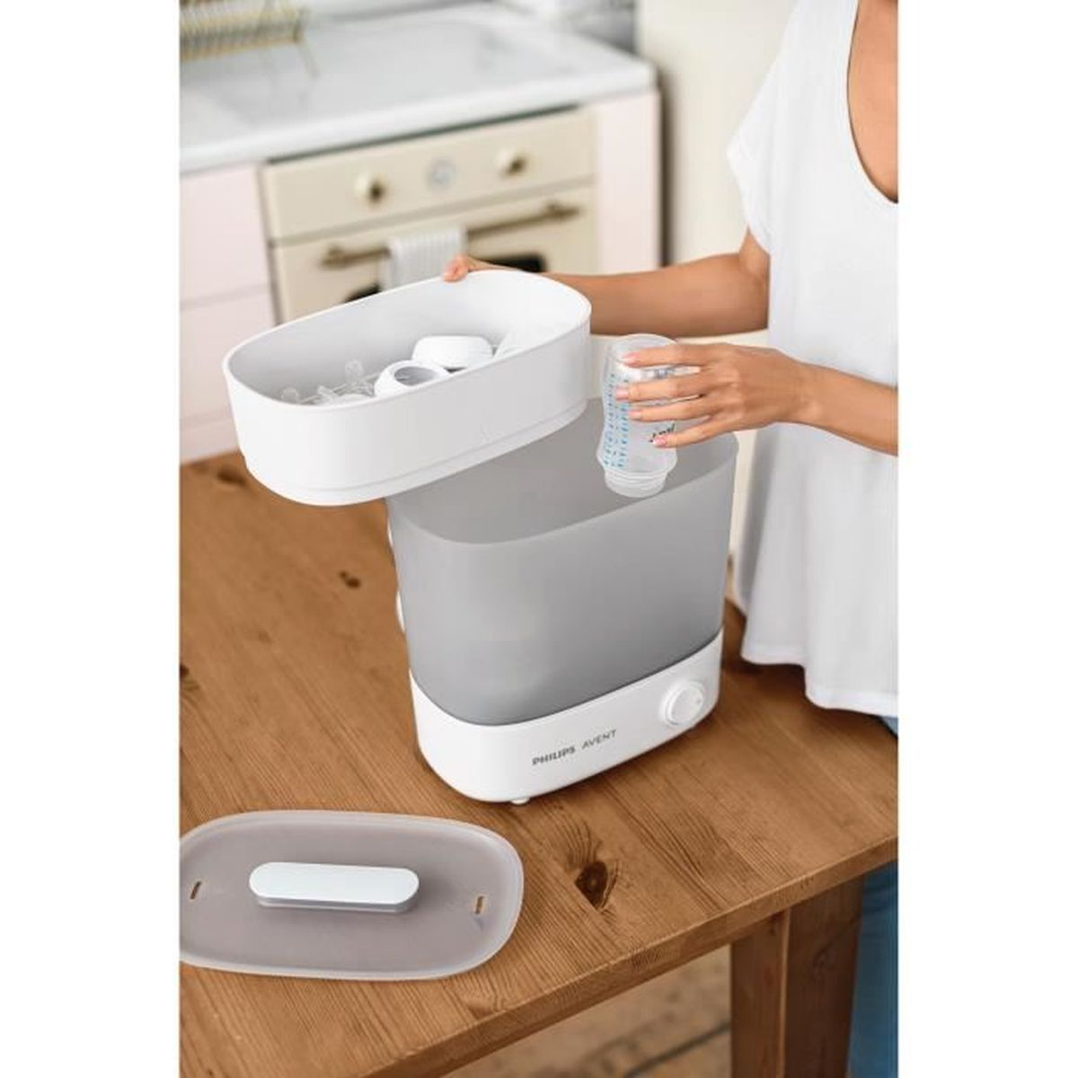 Una mujer usa un esterilizador Philips Avent blanco y gris. El esterilizador está sobre una mesa de madera. Se introduce un biberón.