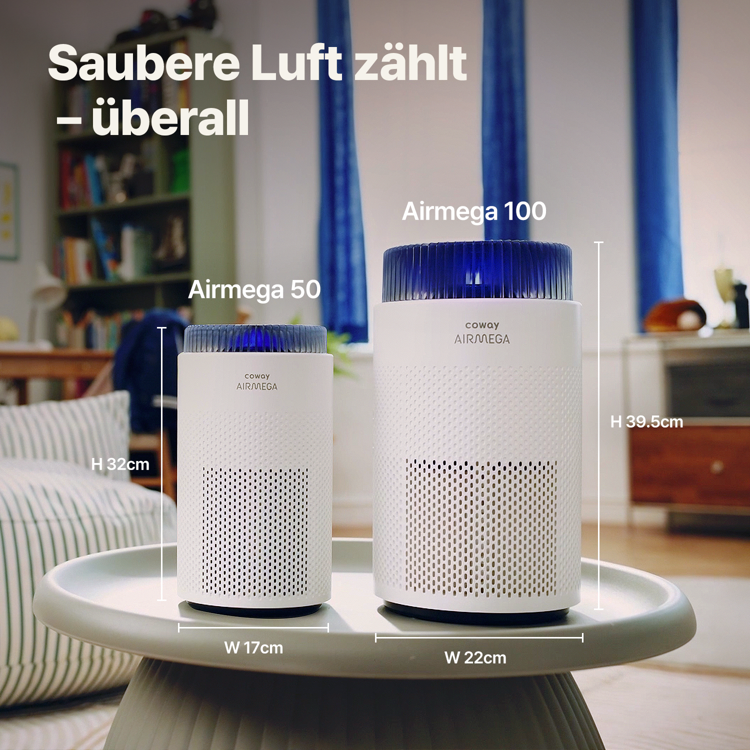 Zwei weiße Luftreiniger, Airmega 50 und 100, auf einem grauen Tisch. Der Hintergrund zeigt ein Bücherregal und einen blauen Vorhang.