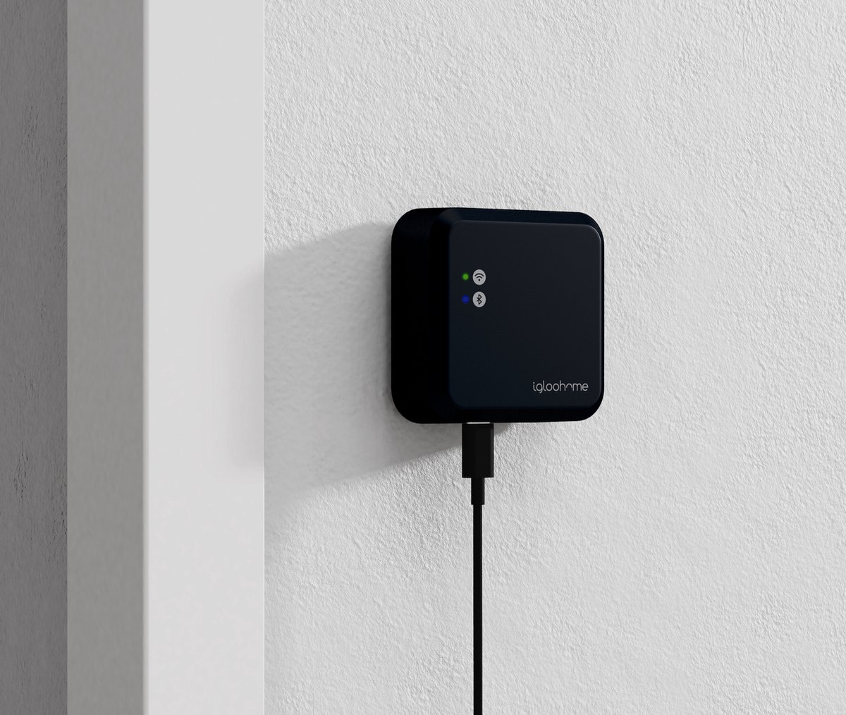 Ein schwarzes quadratisches Gerät ist an einer weißen strukturierten Wand befestigt. Es hat leuchtende Lichter und ein USB-Kabel eingesteckt. Der Markenname ist sichtbar.