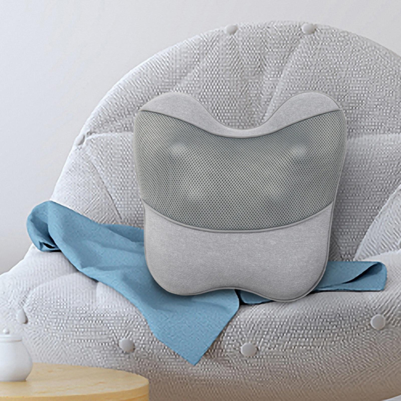 Ein graues Massagekissen auf einem weißen Stuhl mit einem blauen Tuch. Ein kleiner Holztisch und ein weißes Glas sind sichtbar.