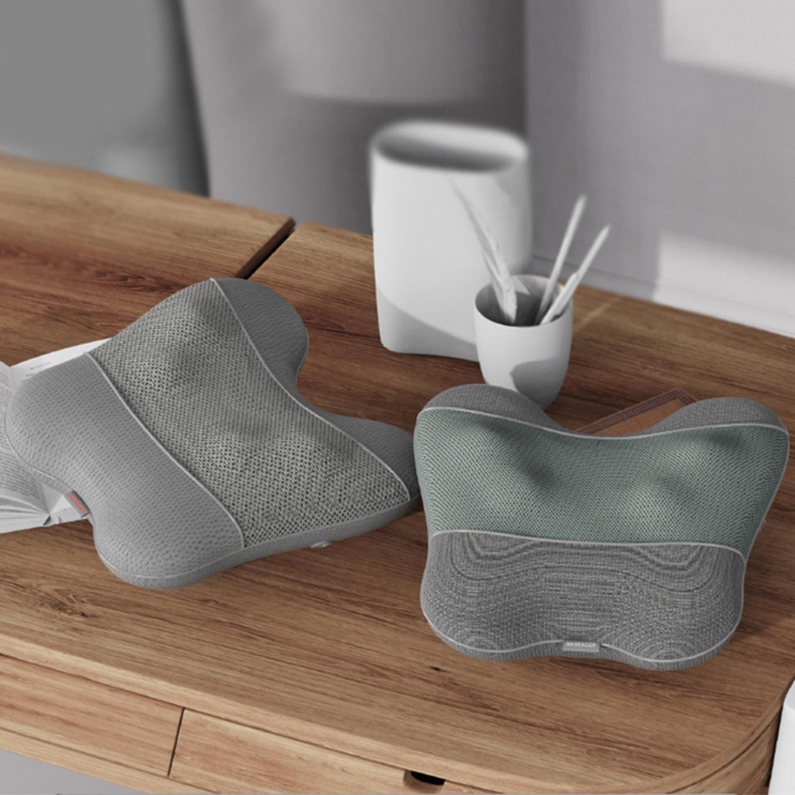 Zwei graue Nackenkissen auf einem Holztisch mit einer weißen Tasse mit weißen Stäben. Der Hintergrund ist unscharf.