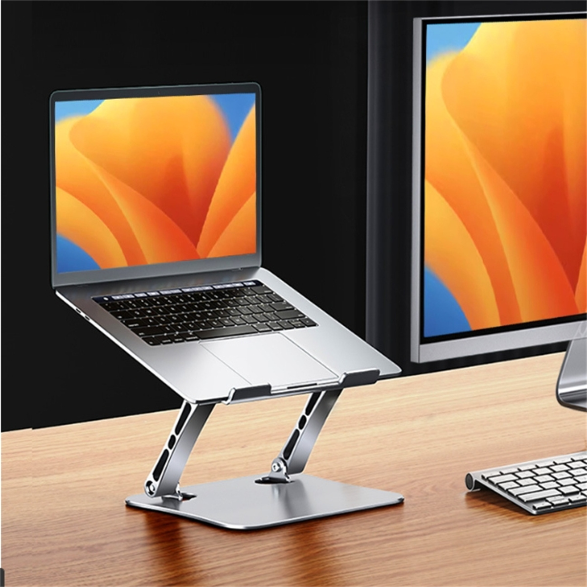 Silberner Laptop auf einem Ständer mit Monitor und Tastatur auf einem Holztisch. Der Laptop zeigt orangefarbene Kunst.