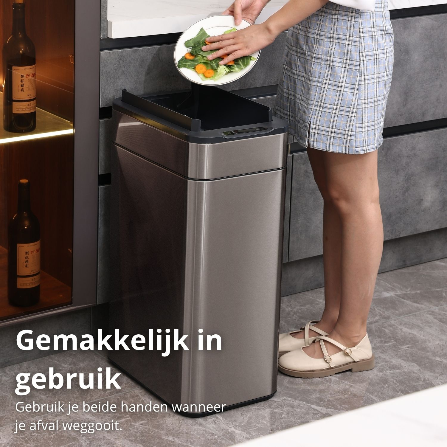 A person throws food waste into a stainless steel trash can. They wear a plaid skirt and shoes. Bottles are in the background.