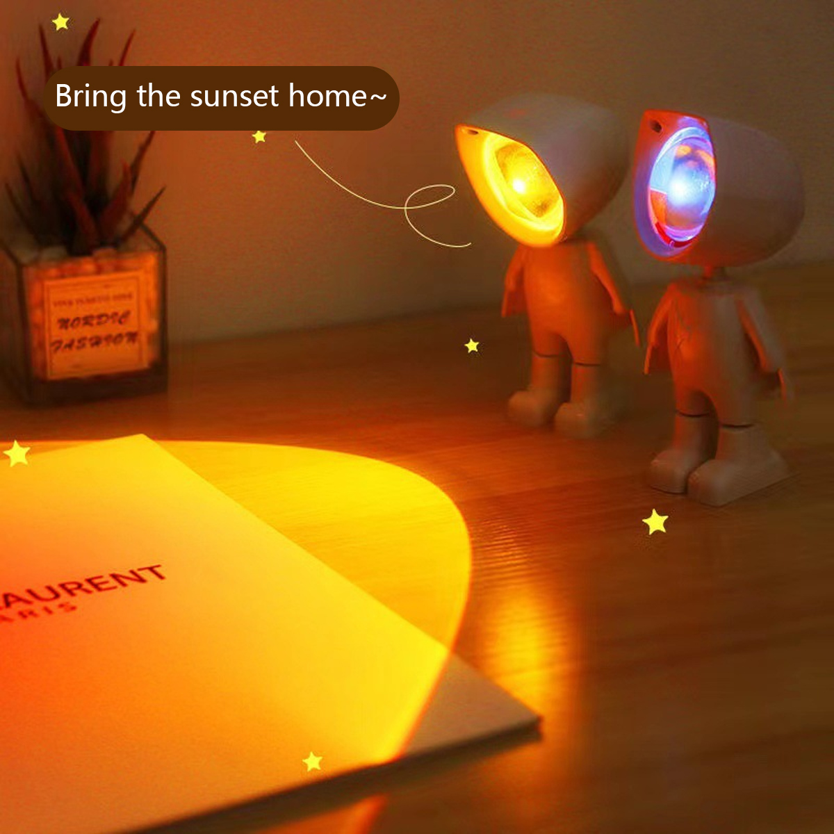 Zwei roboterartige Lampen projizieren orangefarbenes und blaues Licht. Auf der Holzoberfläche befinden sich ein Buch und eine Pflanze. Die Szene ist warm und einladend.