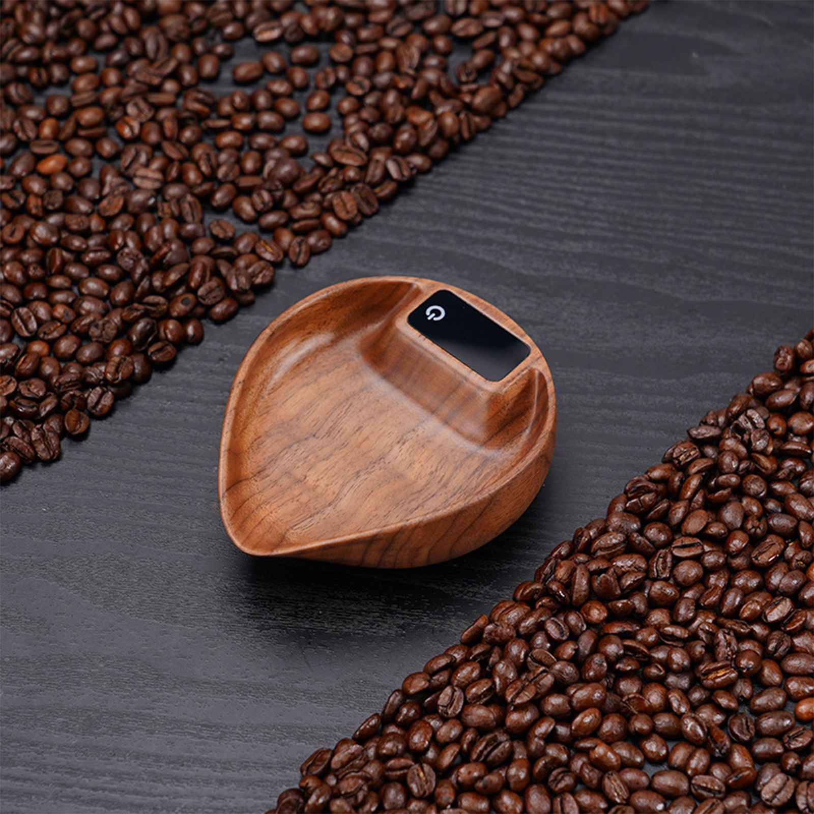 Eine Holzschaufel mit digitaler Anzeige liegt auf einer dunklen Oberfläche, umgeben von Kaffeebohnen. Die Schaufel hat einen Einschaltknopf.