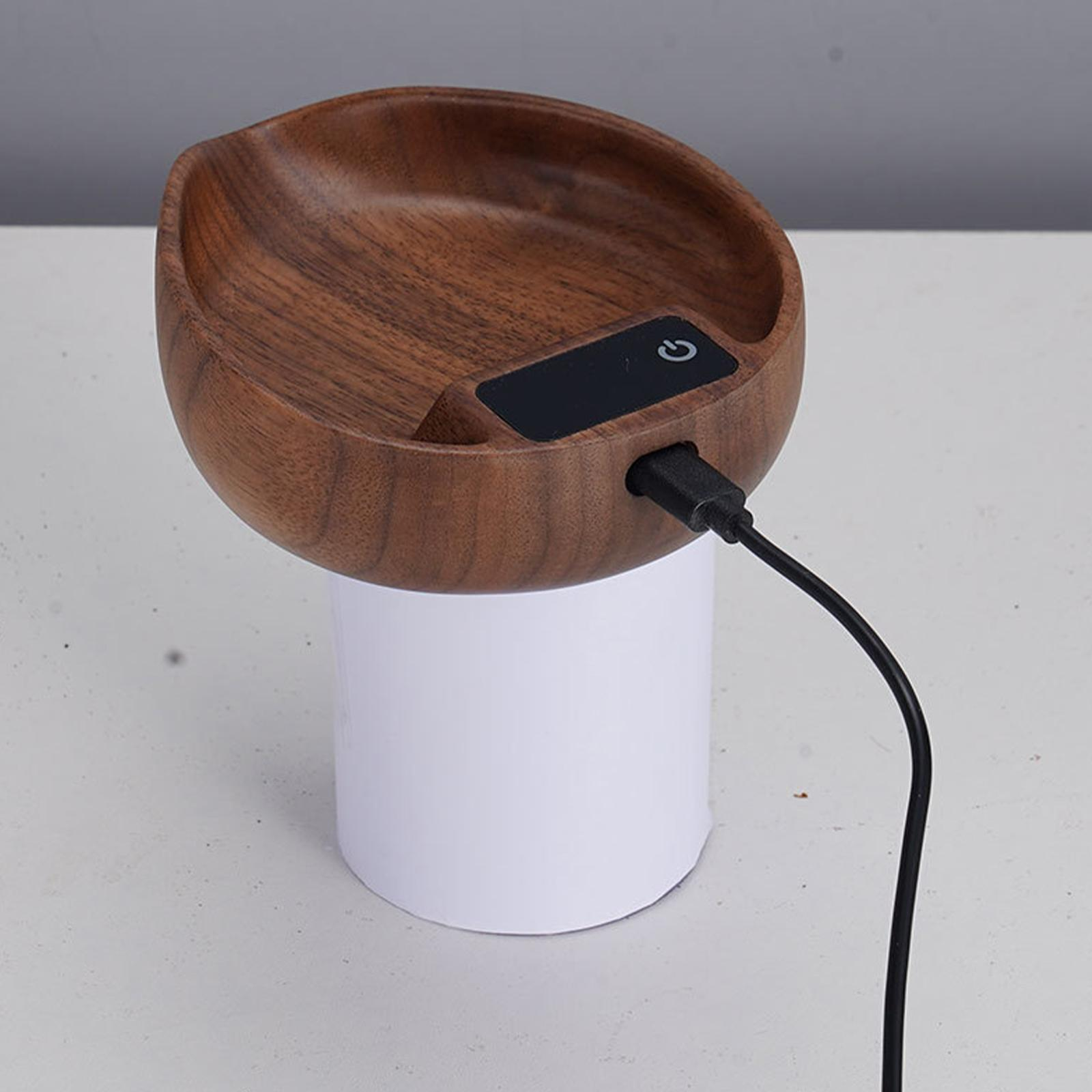 Ein holzförmiges Gerät mit Schüsselform, einem Ein-/Ausschalter, einem weißen zylindrischen Sockel und einem schwarzen Ladekabel.