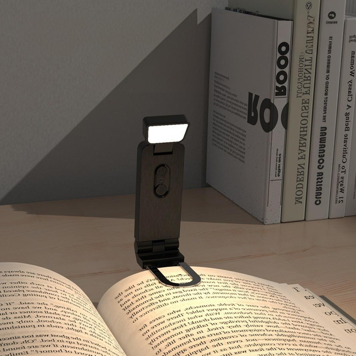 Eine schwarze Buchlampe beleuchtet ein offenes Buch. Bücher sind im Hintergrund. Holzoberfläche.