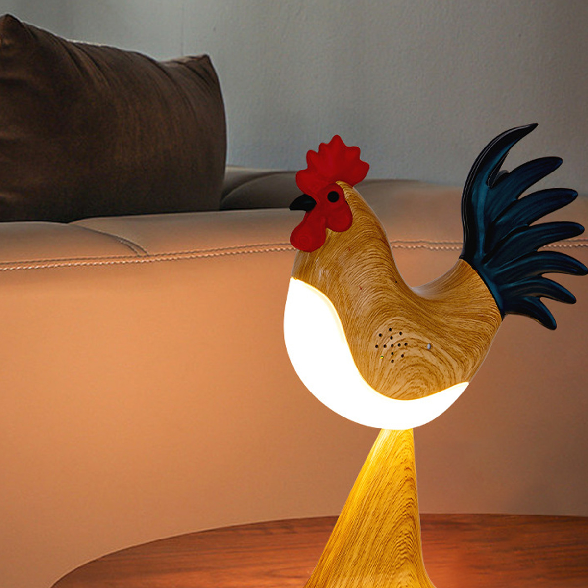 Eine Hahn-Lampe mit rotem Kamm und blauem Schwanz. Sie steht auf einem Holztisch, im Hintergrund ein braunes Sofa.