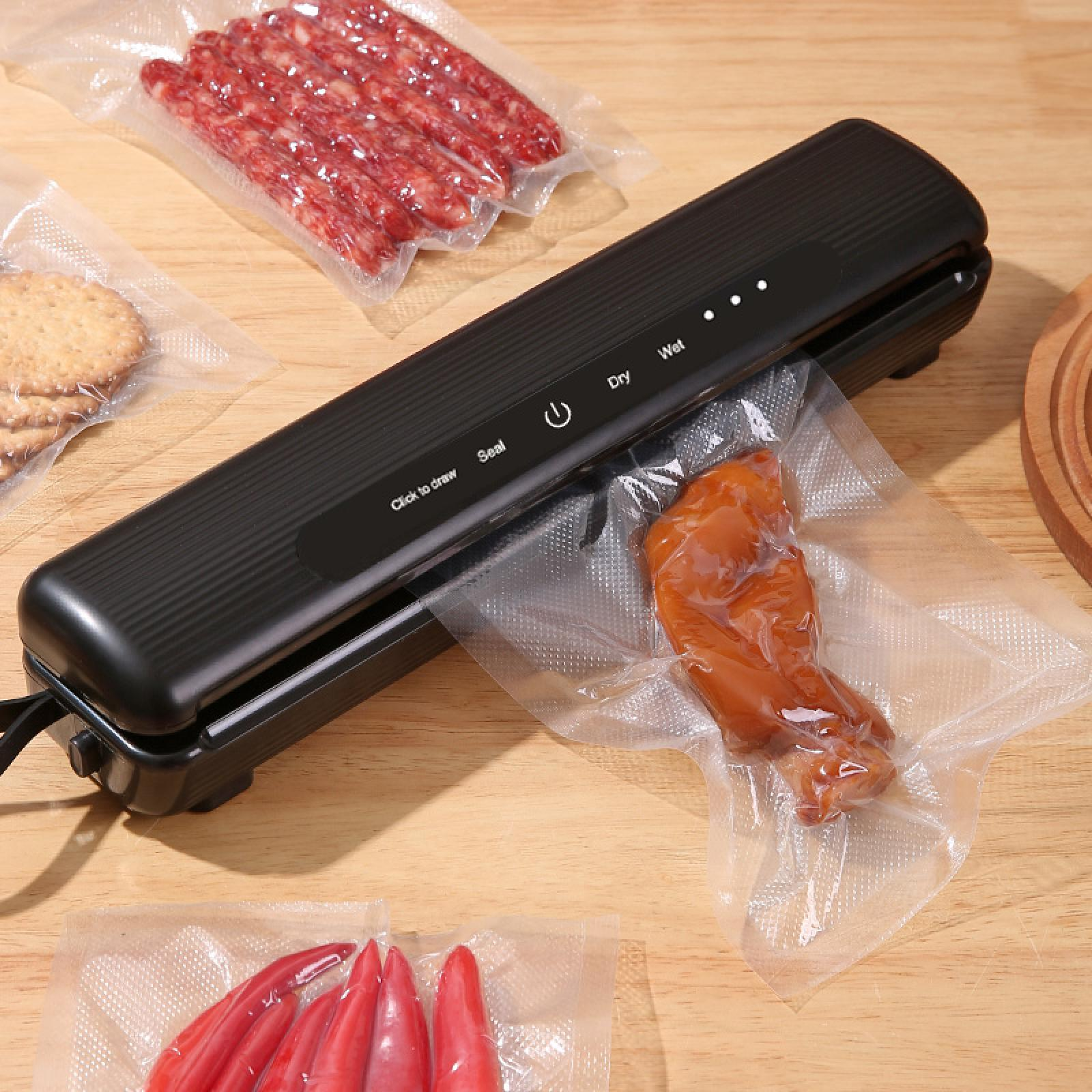 Ein schwarzes Vakuumiergerät mit Lebensmitteln wie Wurst und Paprika in Plastiktüten auf einer Holzoberfläche.