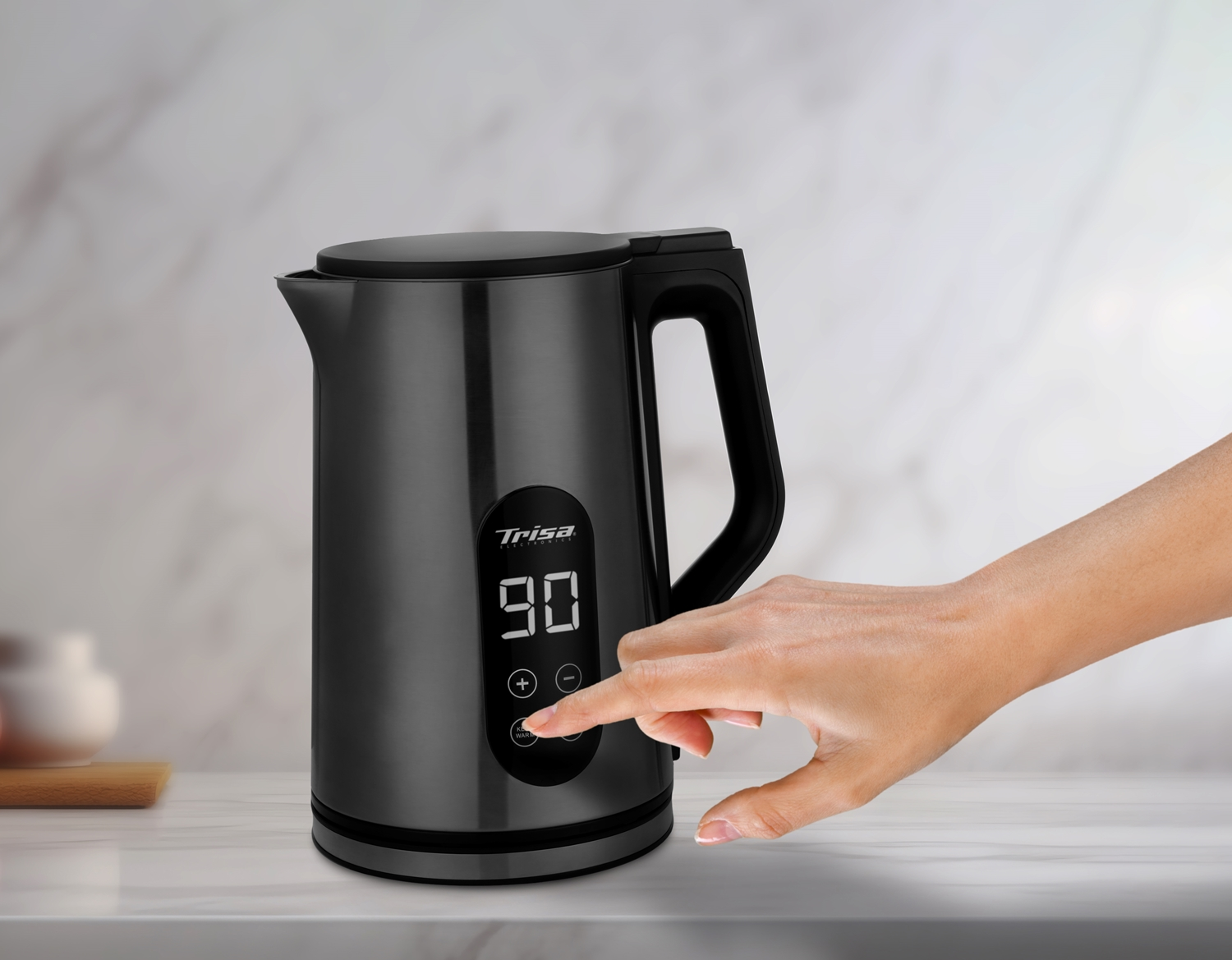 Eine Hand berührt einen schwarzen Wasserkocher mit Digitalanzeige, die 90 Grad anzeigt. Der Hintergrund hat einen Marmoreffekt.