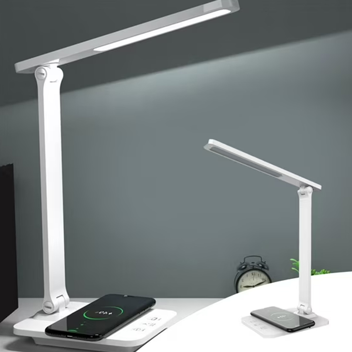 Zwei weiße Schreibtischlampen mit Ladetelefonen. Eine Lampe befindet sich im Vordergrund, eine andere im Hintergrund. Eine Uhr und eine Wand sind ebenfalls sichtbar.