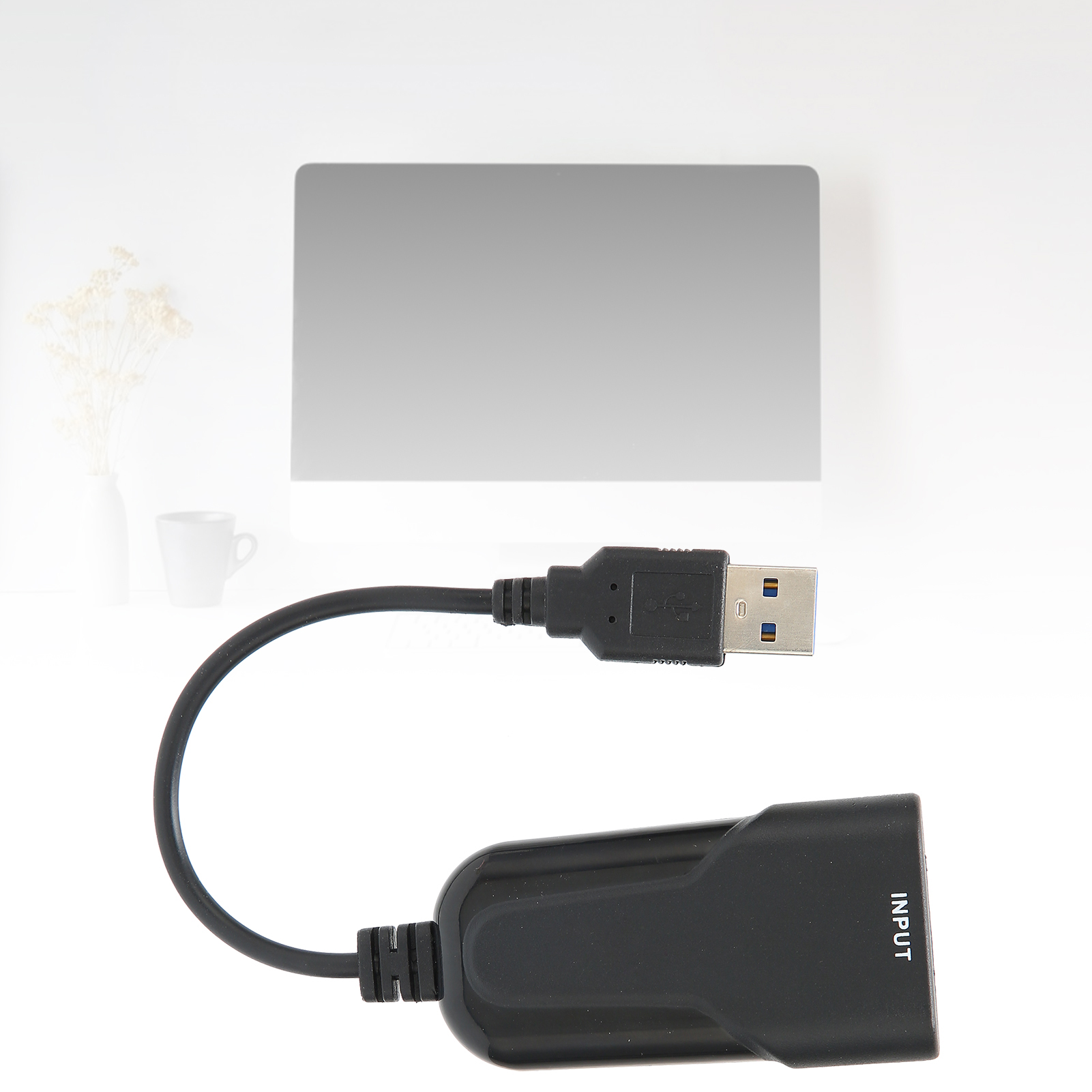 Ein schwarzes USB-Adapterkabel mit einem rechteckigen Anschluss mit der Aufschrift INPUT liegt auf einer weißen Oberfläche. Im Hintergrund eine graue Form.