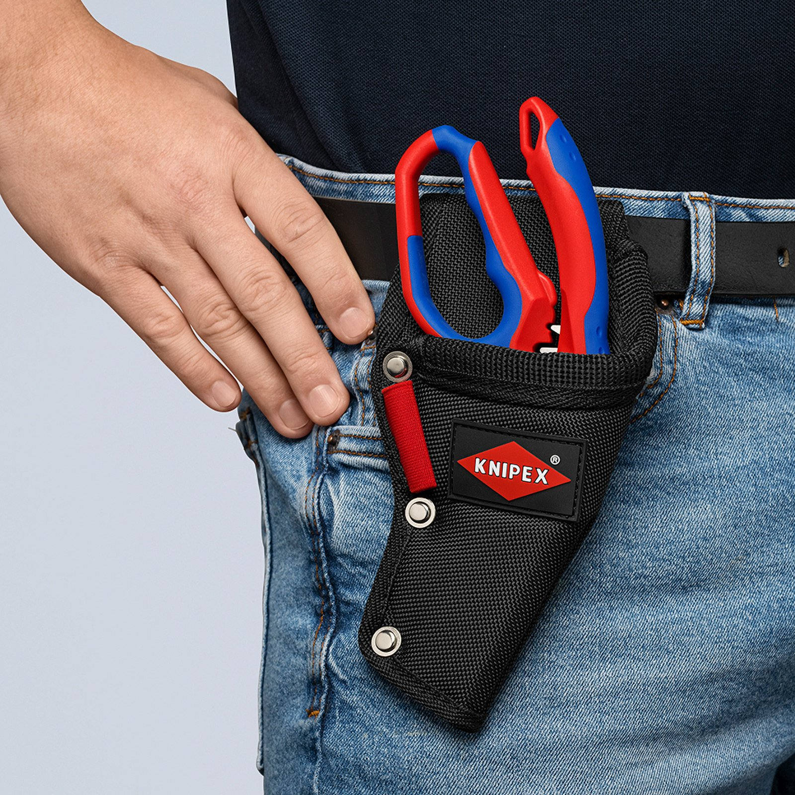 Die Taille einer Person mit einem schwarzen Werkzeughalter, der rot-blaue Zangen enthält. Auf dem Halter befindet sich ein Knipex-Logo.