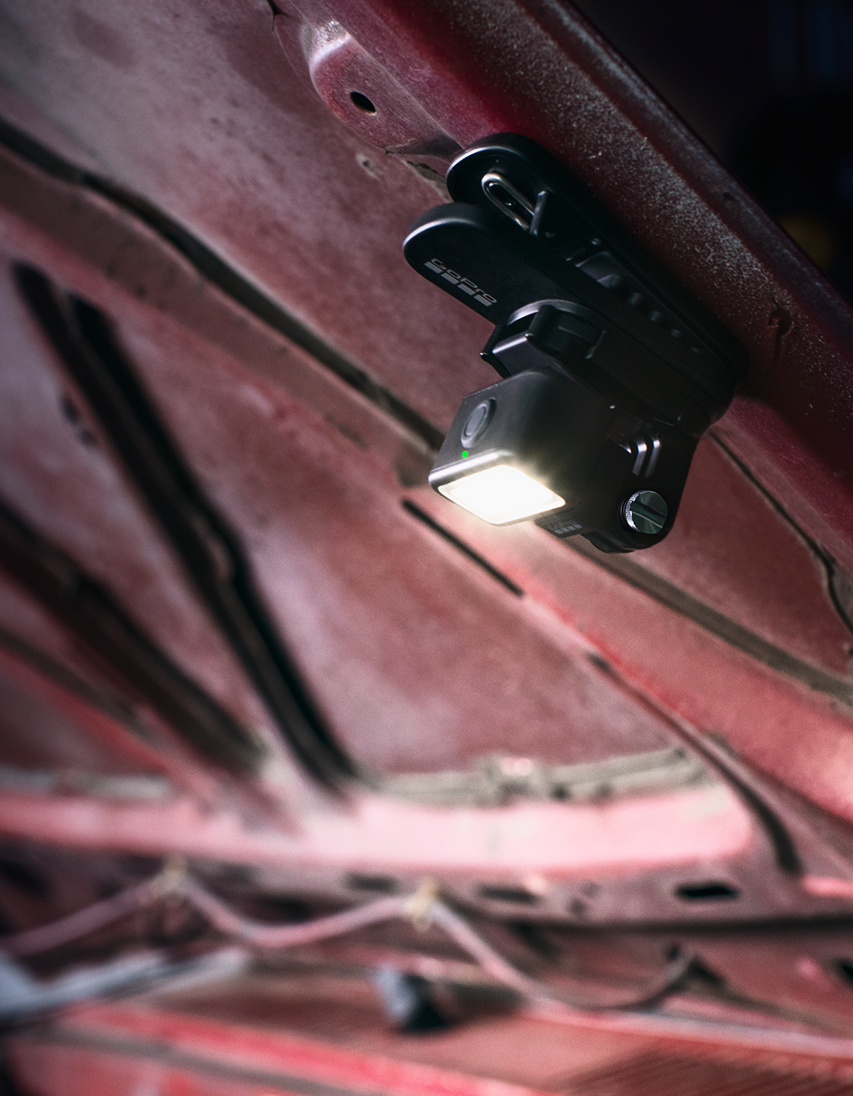 Czarna lampa GoPro jest przymocowana do wewnętrznej strony czerwonej maski samochodu. Światło jest włączone i oświetla obszar.