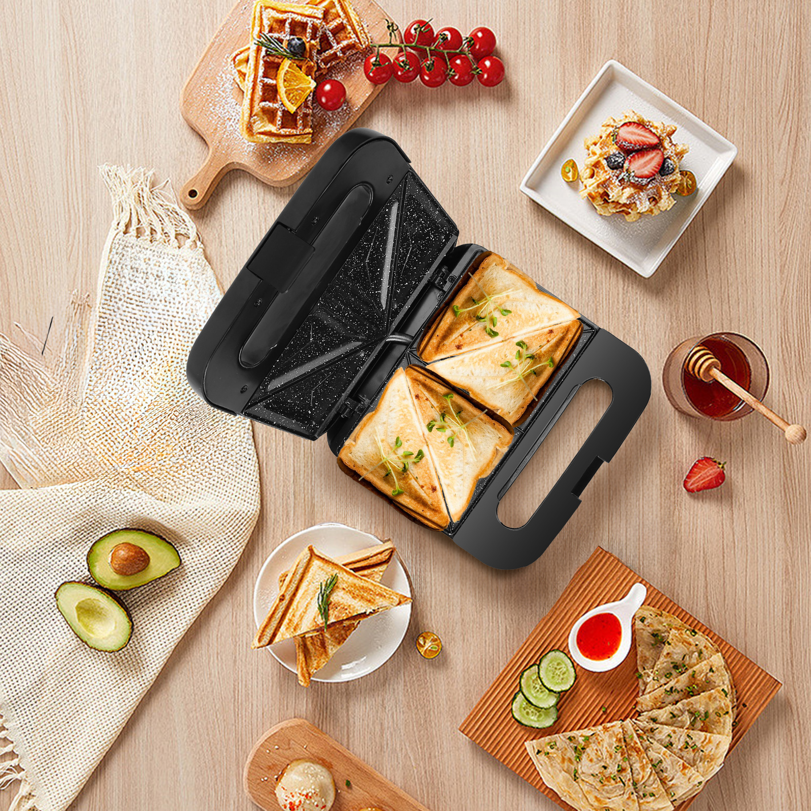 Una sandwichera abierta con sándwiches tostados. Gofres, aguacate y otros alimentos la rodean sobre una mesa de madera.