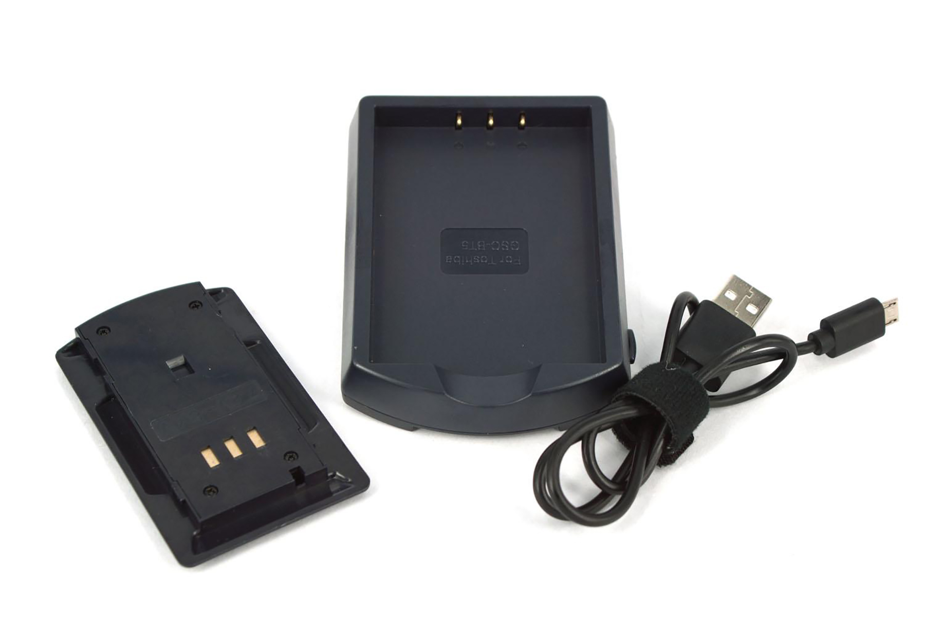 Ein schwarzes Ladegerät, ein Akku und ein USB-Kabel auf weißem Untergrund. Das Ladegerät ist rechteckig mit drei goldenen Pins.
