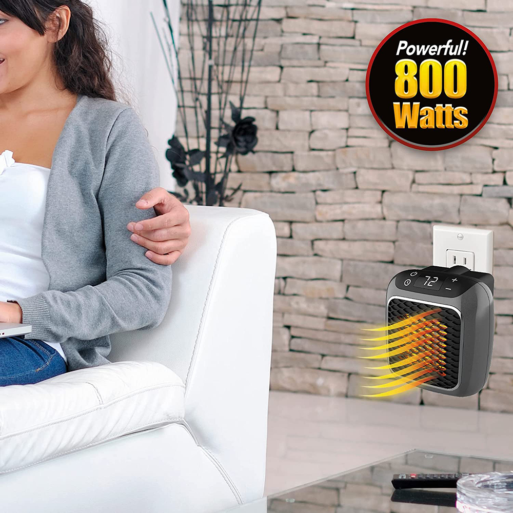 Eine Frau sitzt auf einem weißen Sofa. Ein kleiner schwarzer Heizlüfter ist in die Wand gesteckt. Ein Schild zeigt 800 Watt an.