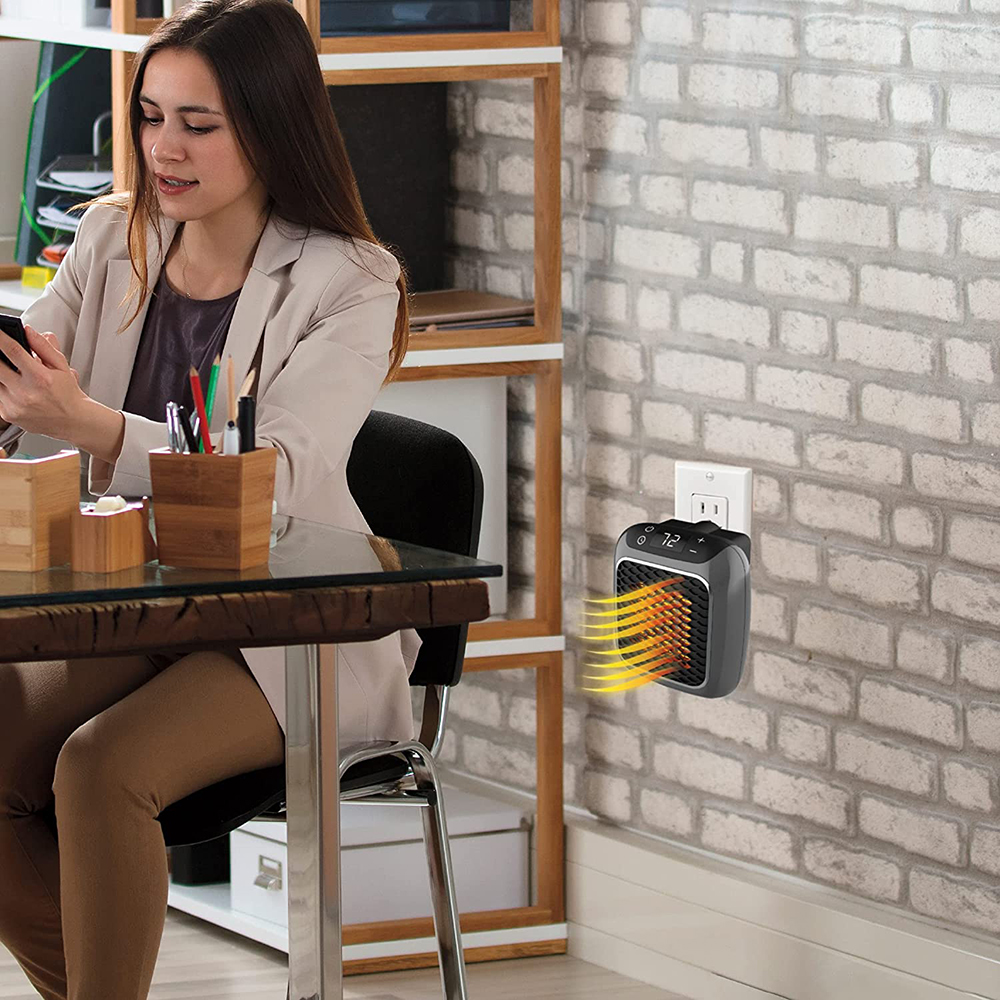 Eine Frau sitzt an einem Schreibtisch und benutzt ein Telefon. Ein kleiner Heizlüfter ist an der Wand angeschlossen. Ein Bücherregal ist im Hintergrund zu sehen.